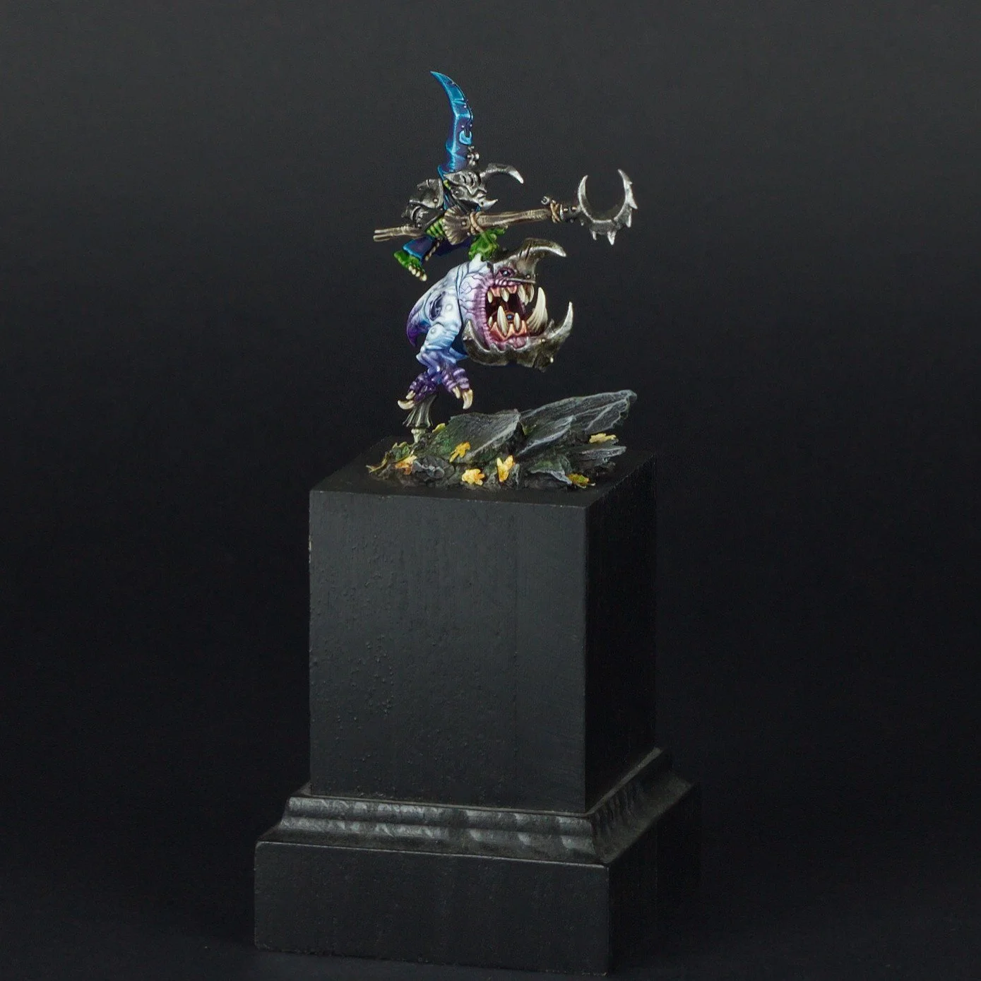 A miniature fantasy figurine of a warrior riding a monstrous creature, displayed on a black pedestal against a plain black background.