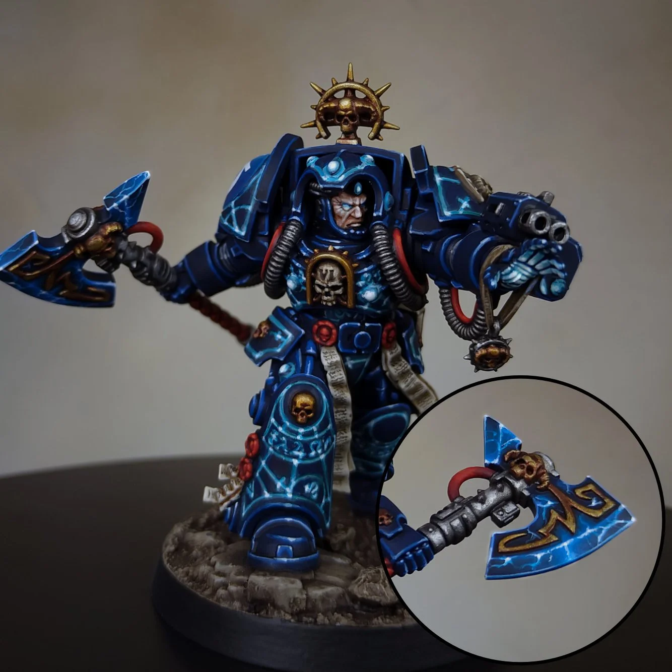 A painted miniature of a futuristic armored warrior wielding a large axe and a gun. The armor is primarily blue with skull and lightning motifs, and the warrior wears a helmet with a skull emblem on top. The figure stands on a textured base.