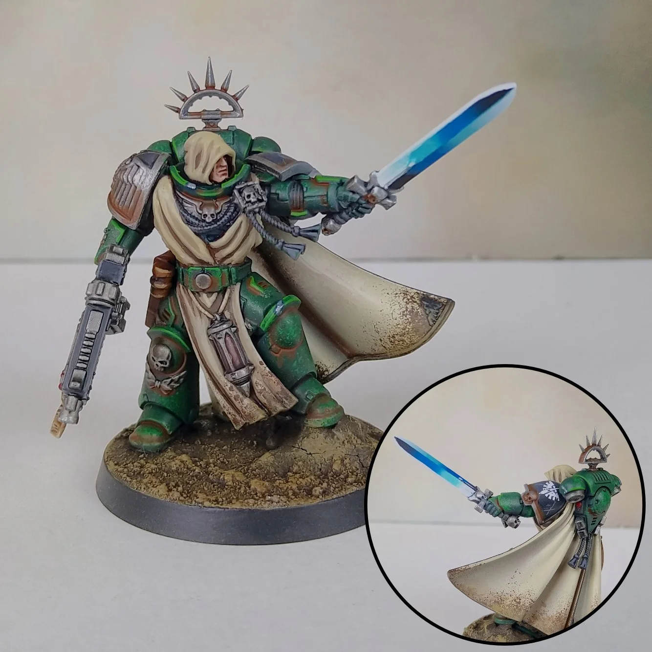 A detailed miniature figurine of a medieval warrior in green armor, wielding a sword with a blue blade and a pistol, standing on a scenic base with a beige and brown cloak and skull motifs.