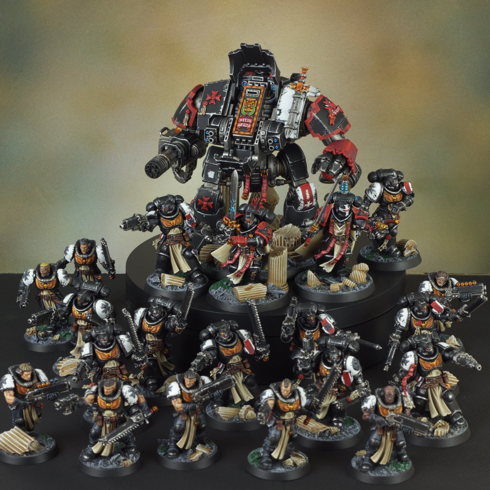 A collection of Warhammer 40k miniatures, including a large robotic war machine and smaller soldiers with black armor, white and beige cloaks, and weapons, arranged on a black circular display with scattered debris and ruins.