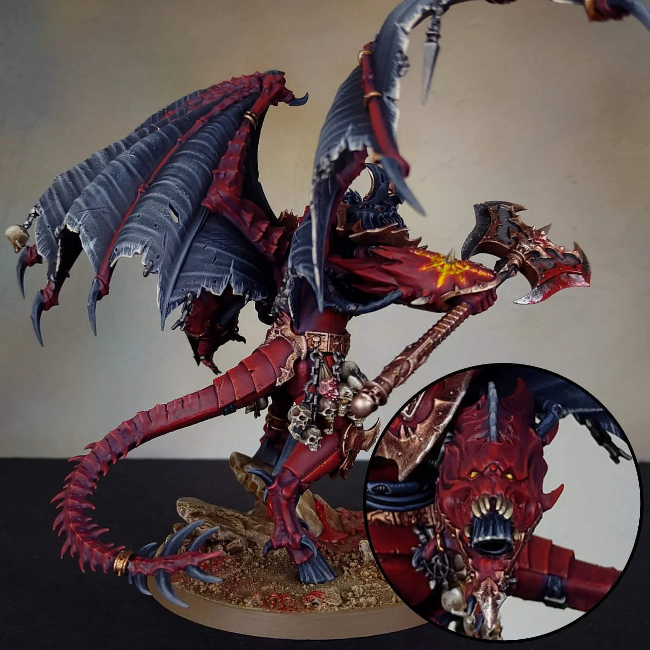 A detailed painted miniature of a demonic creature with dragon-like features, red and black armor, large wings, and a spiked tail, holding an axe and standing on a textured base.