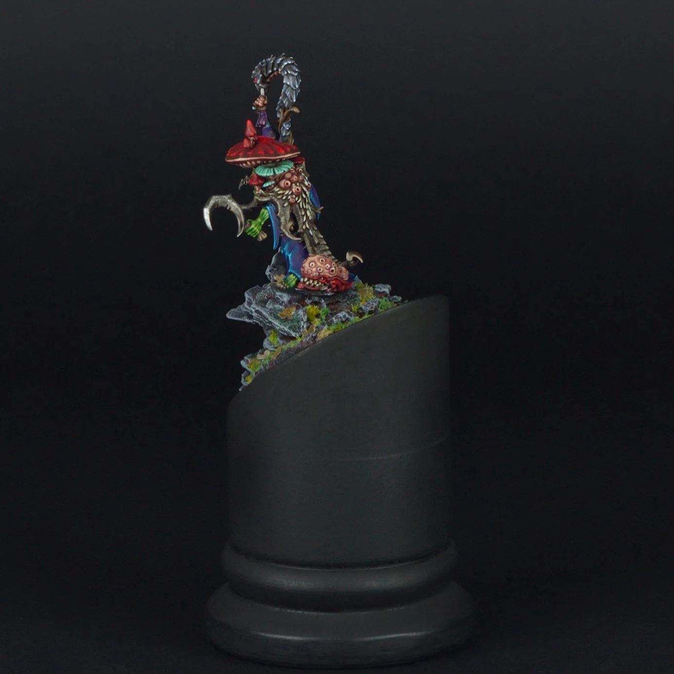 Colorful fantasy miniature figurine on black display pedestal against black background.