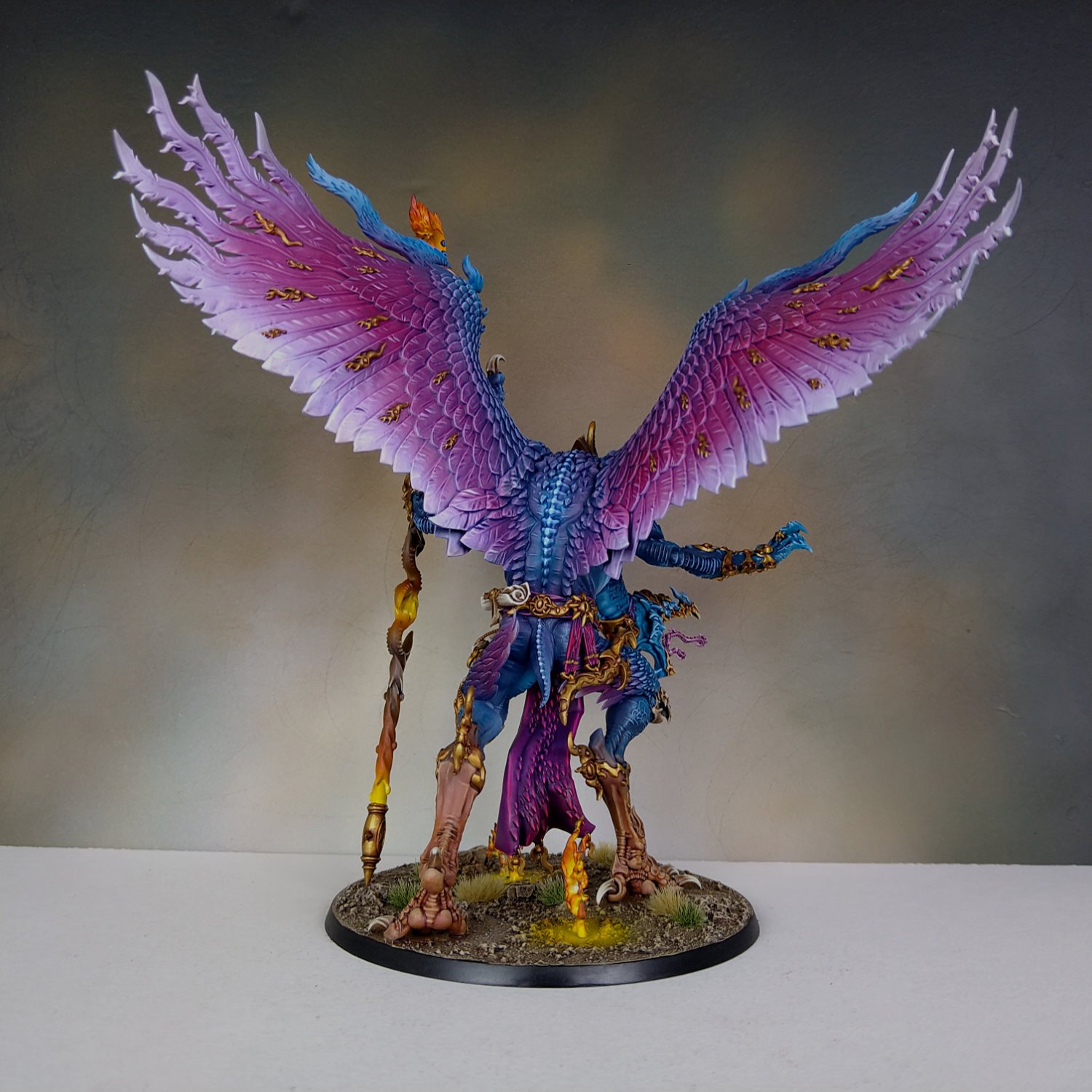 Colorful miniature fantasy creature with large pink and purple wings, intricate armor, and a staff, standing on a base with grass and terrain.