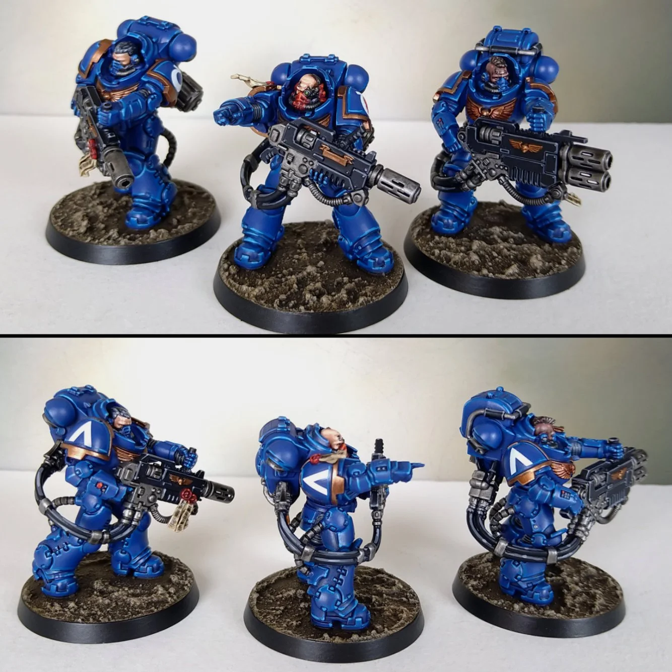 Set of four painted miniature space marines in blue armor, equipped with guns, standing on round bases with textured ground.