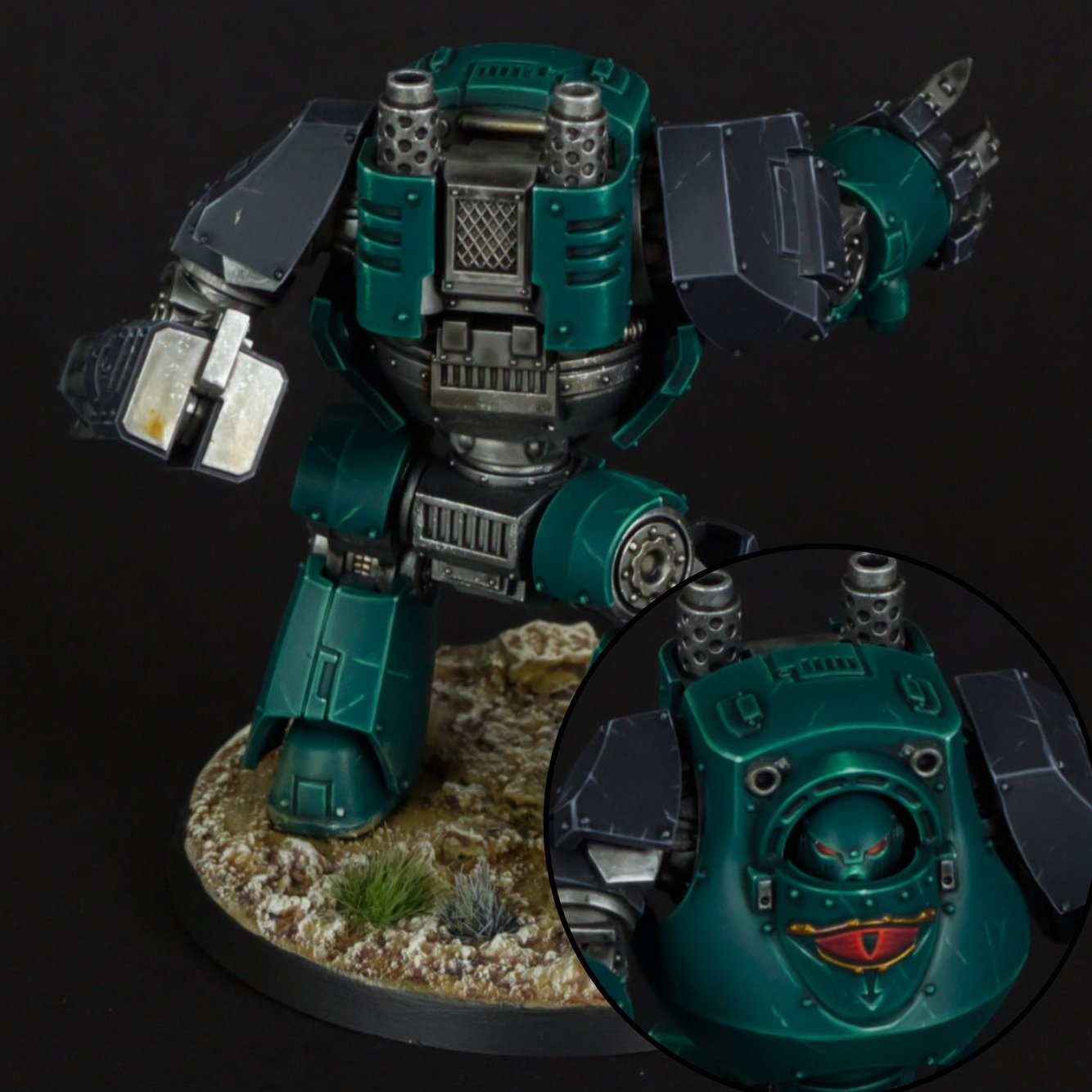 A detailed model of a teal robot with armor and mechanical parts, standing on a base with small plants and rocks, set against a black background. The robot's chest and shoulder armor are prominent, and an inset shows the robot's head with a fierce fa