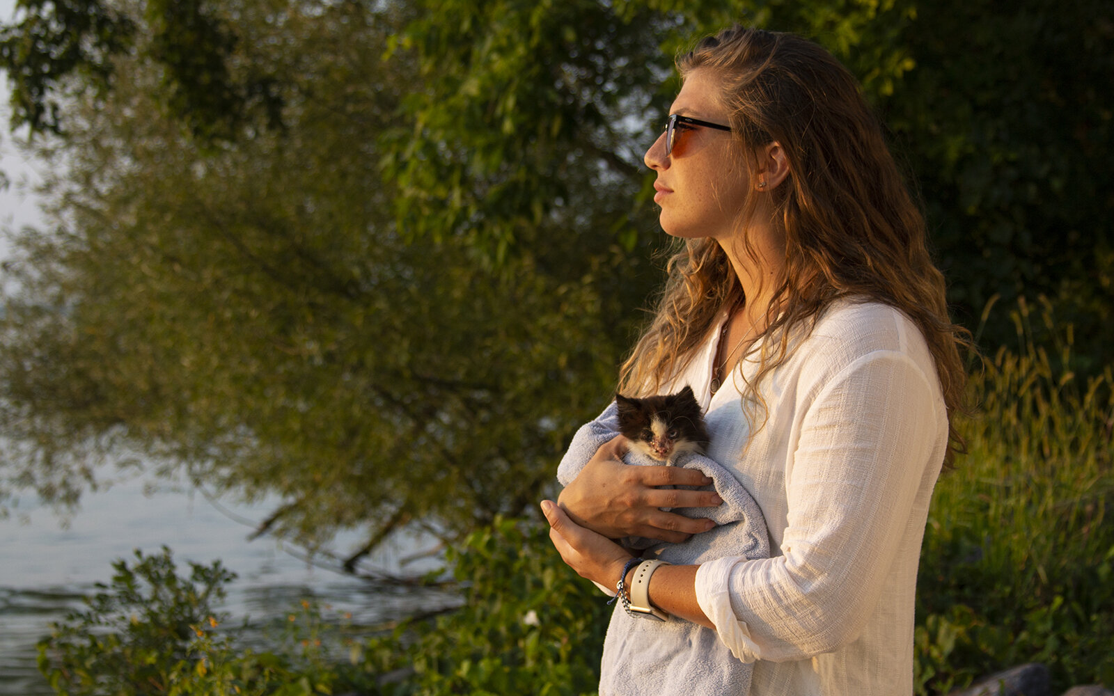 Portrait of a woman looking out onto a lake while she's holding a kitten she found left on the side of the road. Upstate New York Photographer.