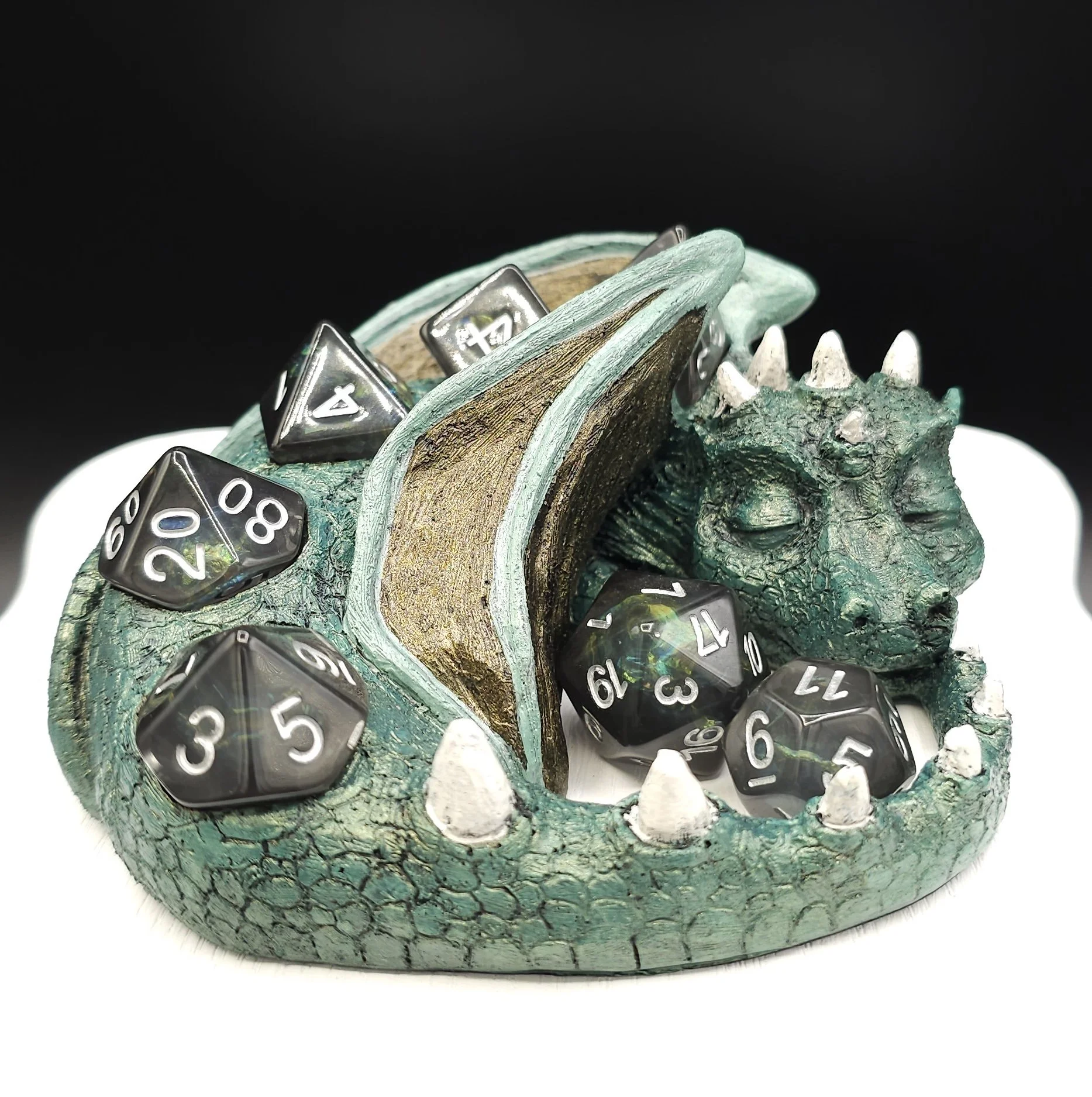 A dragon with several black polyhedral dice resting on it, all set against a dark background.