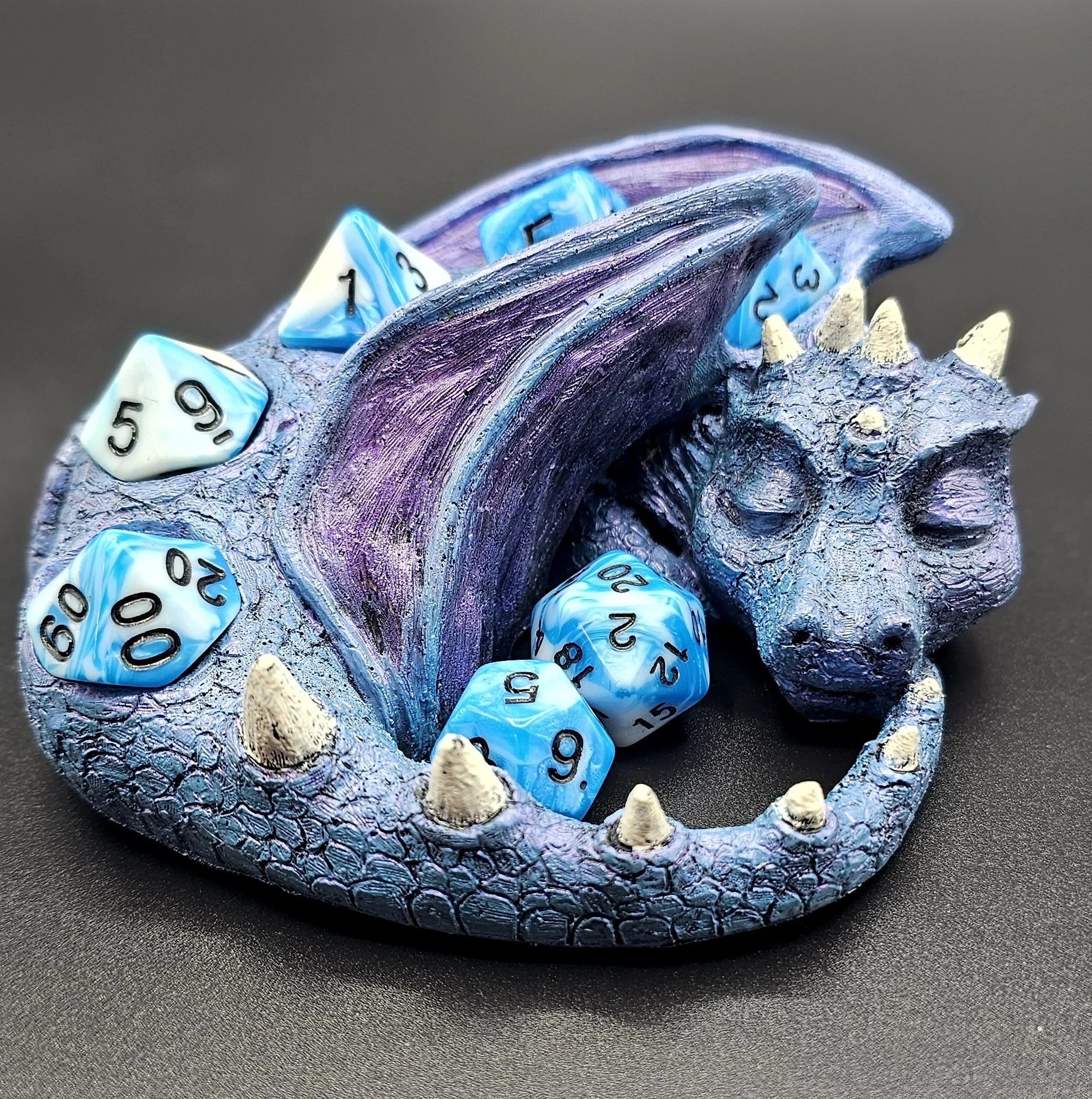 A blue and purple dragon-themed dice holder with several polyhedral dice, including a ten-sided die showing the number 60, a twenty-sided die showing 15, and other dice with numbers.