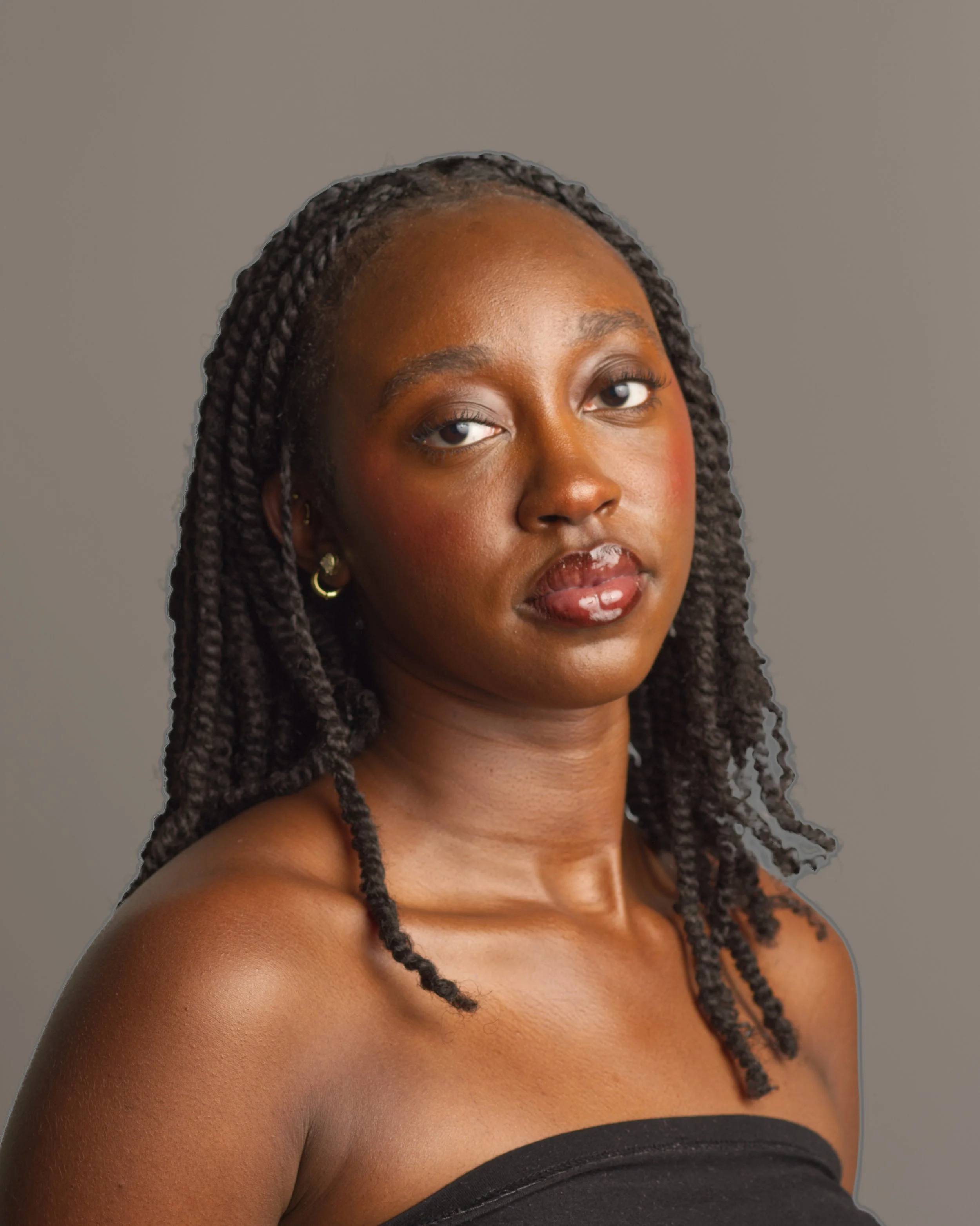Close-up portrait of a woman with dark skin and braided hair, wearing earrings, with a neutral background.