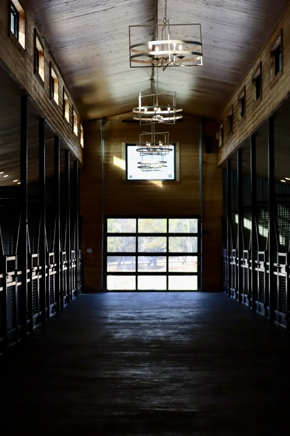 Interior view of a modern wooden hallway with large glass windows, hanging circular chandeliers, and a wooden ceiling.