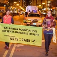 2 people in a parade holding a Kalapriya banner that says Arts in the Dark