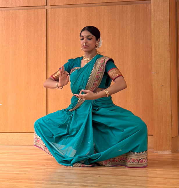 Children in classroom raising their hands, with teacher in the background.