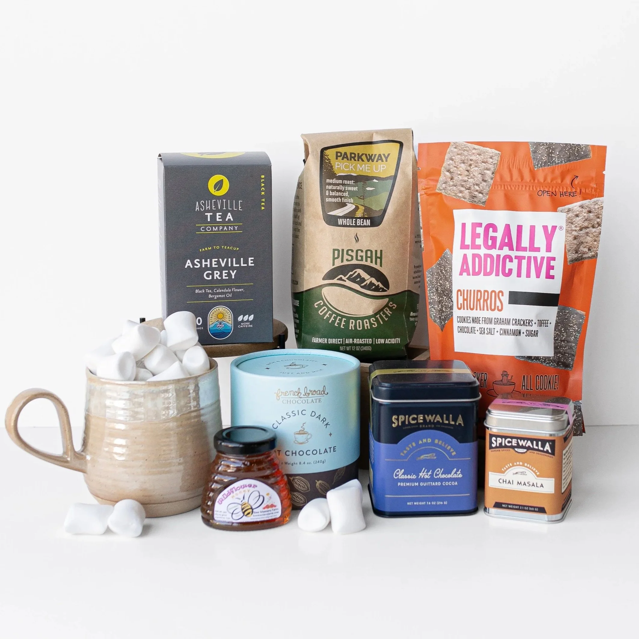 Assortment of Asheville tea, whole-bean coffee, churro cookies, hot chocolate, chai masala, honey, marshmallows, and a ceramic mug