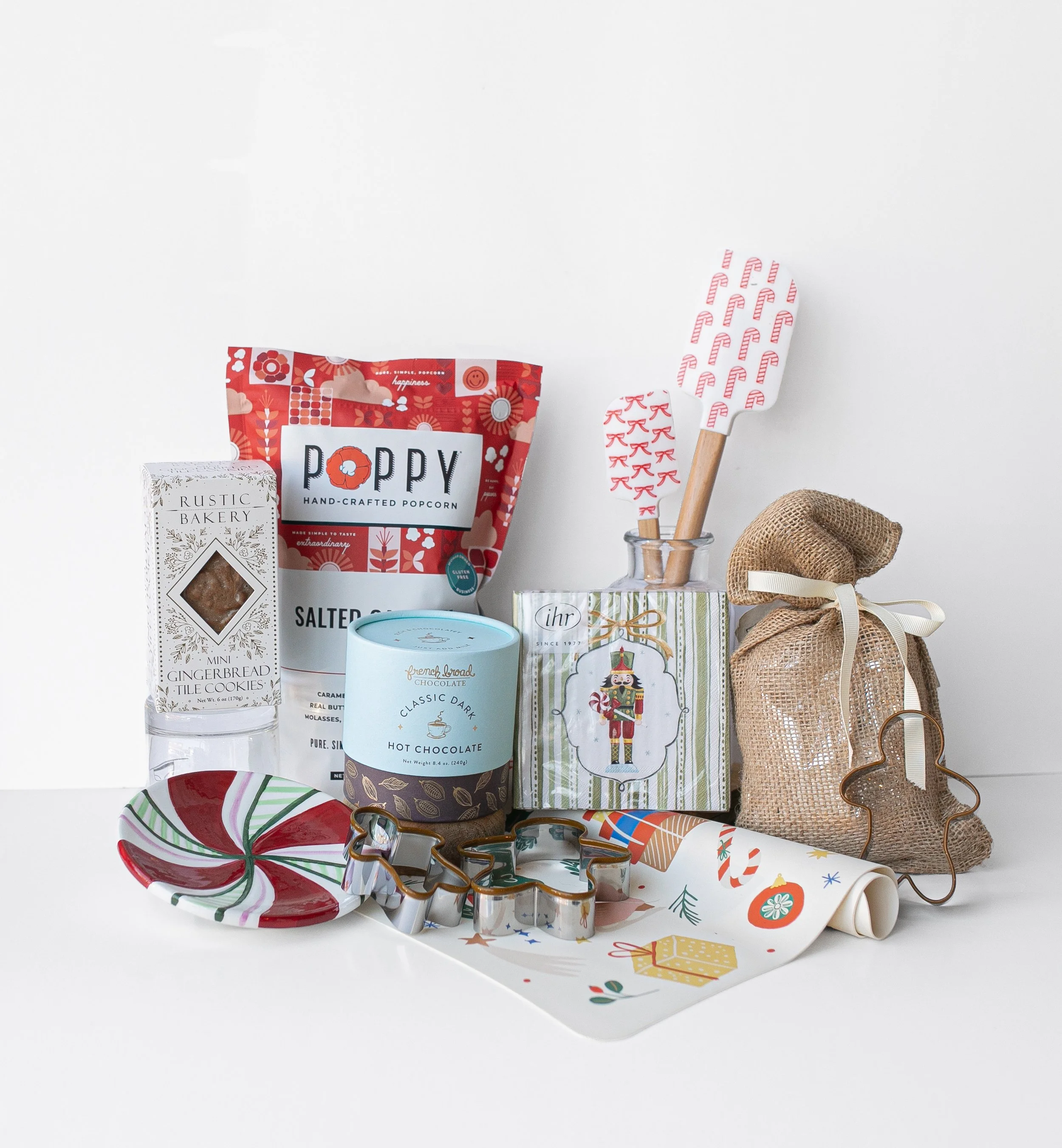 Festive holiday gift assortment with popcorn, gingerbread cookies, hot chocolate, wrapped presents, Christmas ornaments, spatulas, and burlap gift bags