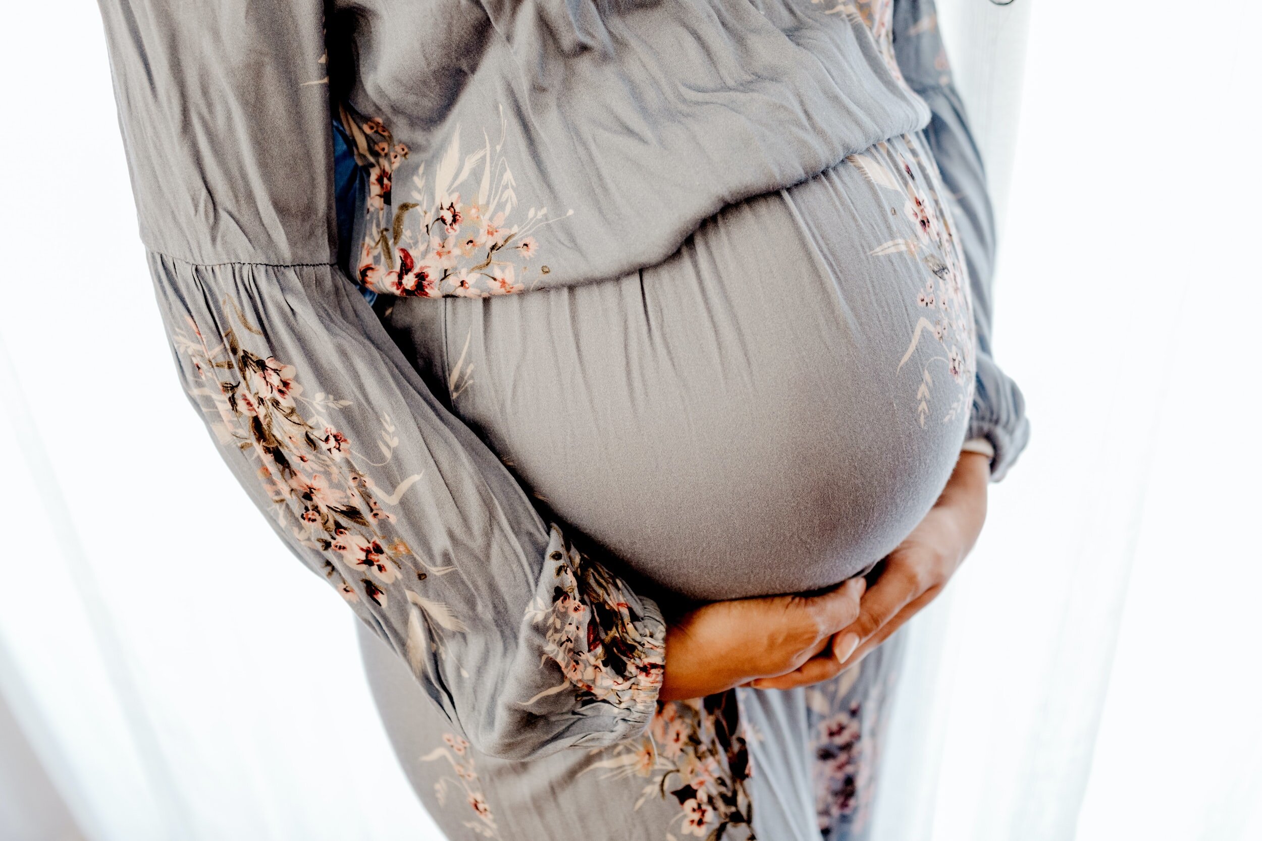 Pregnant woman in floral dress holding her belly.