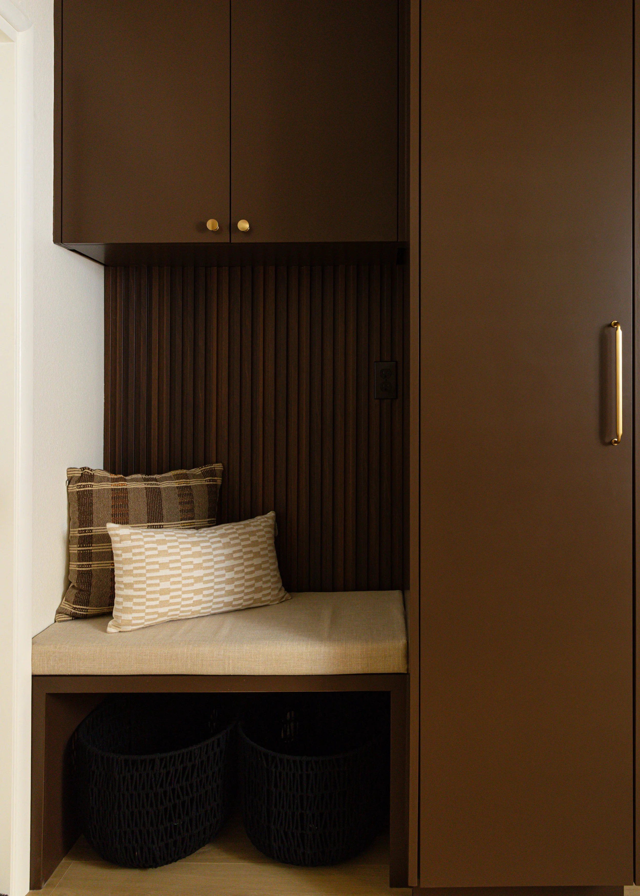 Built-in laundry room bench with dark brown cabinetry, walnut slat paneling and concealed storage in the Canyon Lane remodel.
