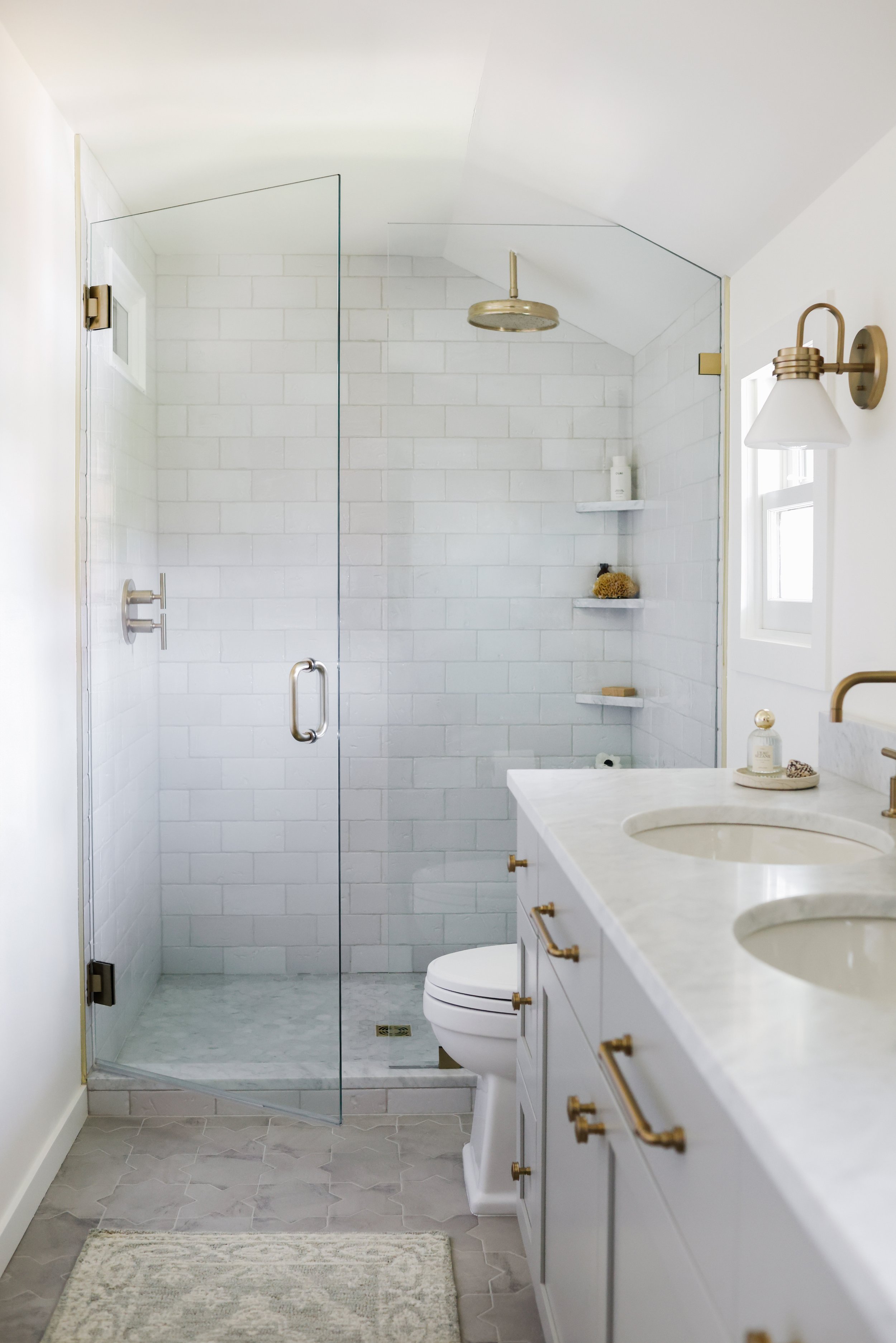 Light-filled bathroom remodel with glass shower, marble surfaces and brass fixtures by Ashley Kiely Living in Portland, Oregon.