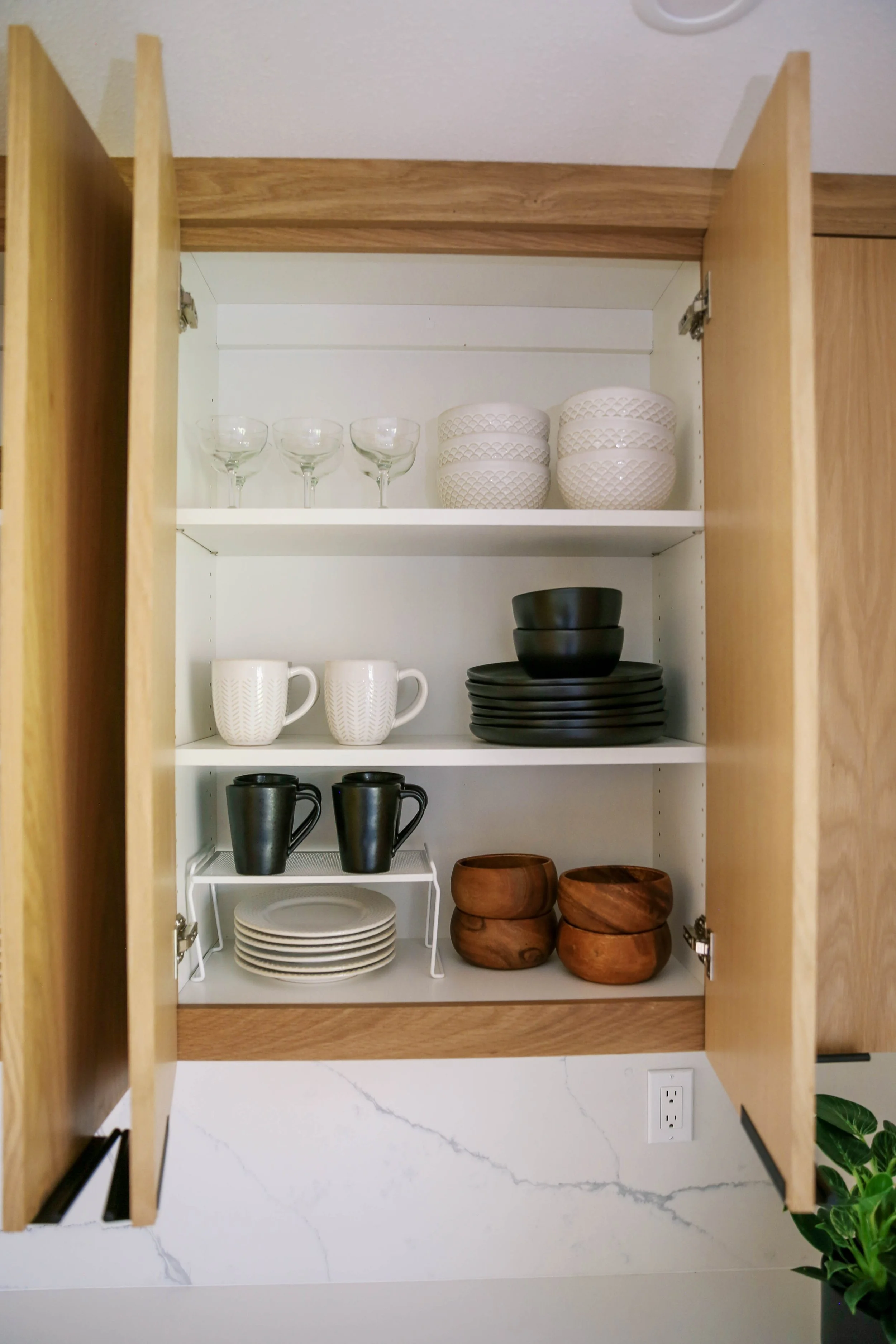 Kitchen cabinet unpacked and organized with plates, bowls, mugs and glassware for a move-in-ready home.