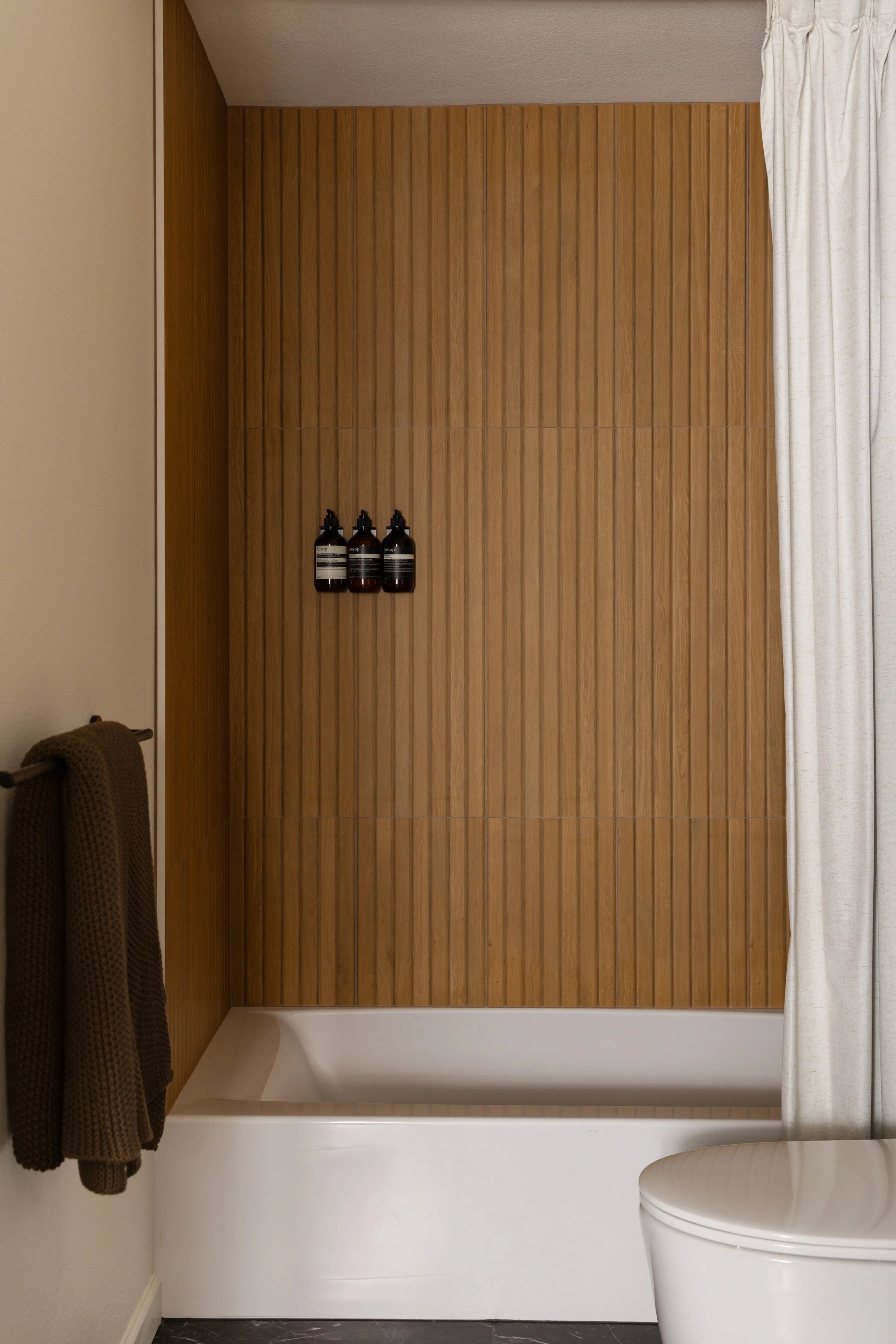 Hall bathroom with terrazzo-look wall tile, wood-look shower tile, floating walnut vanity and matte black accents.