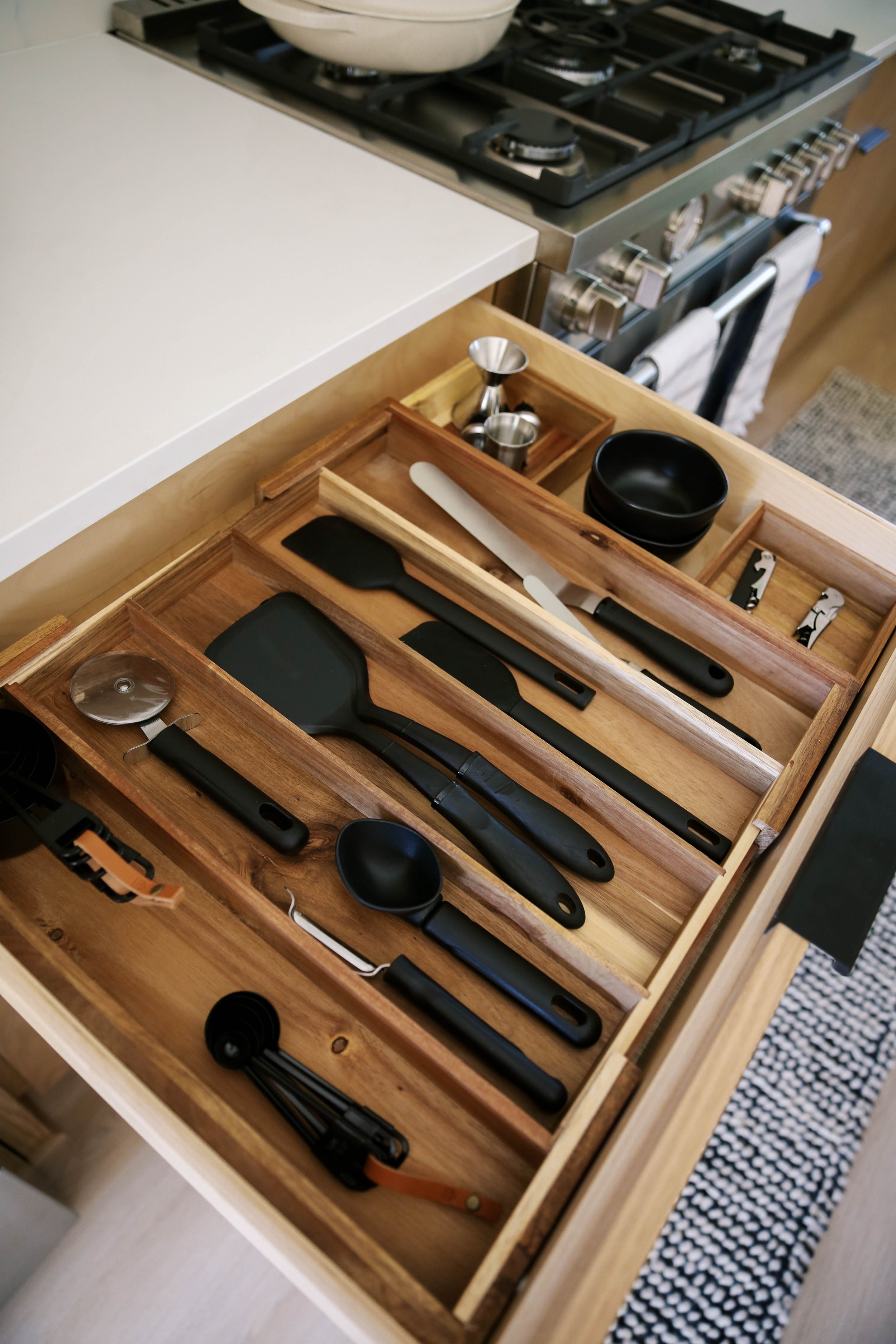 Kitchen utensil drawer arranged with custom wood dividers beside the range during complete home setup.