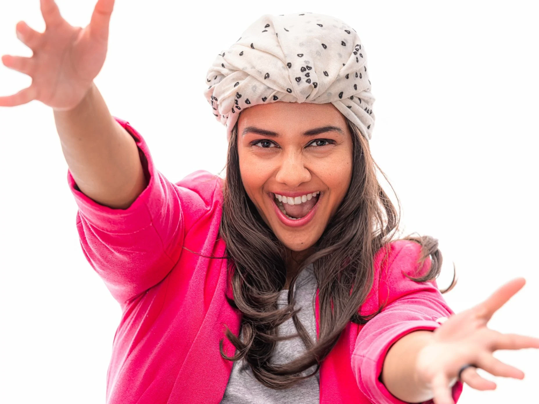 A woman smiling and reaching towards the camera, wearing a pink jacket, a gray shirt, and a rolled-up headscarf with black paw prints on it, against a white background.