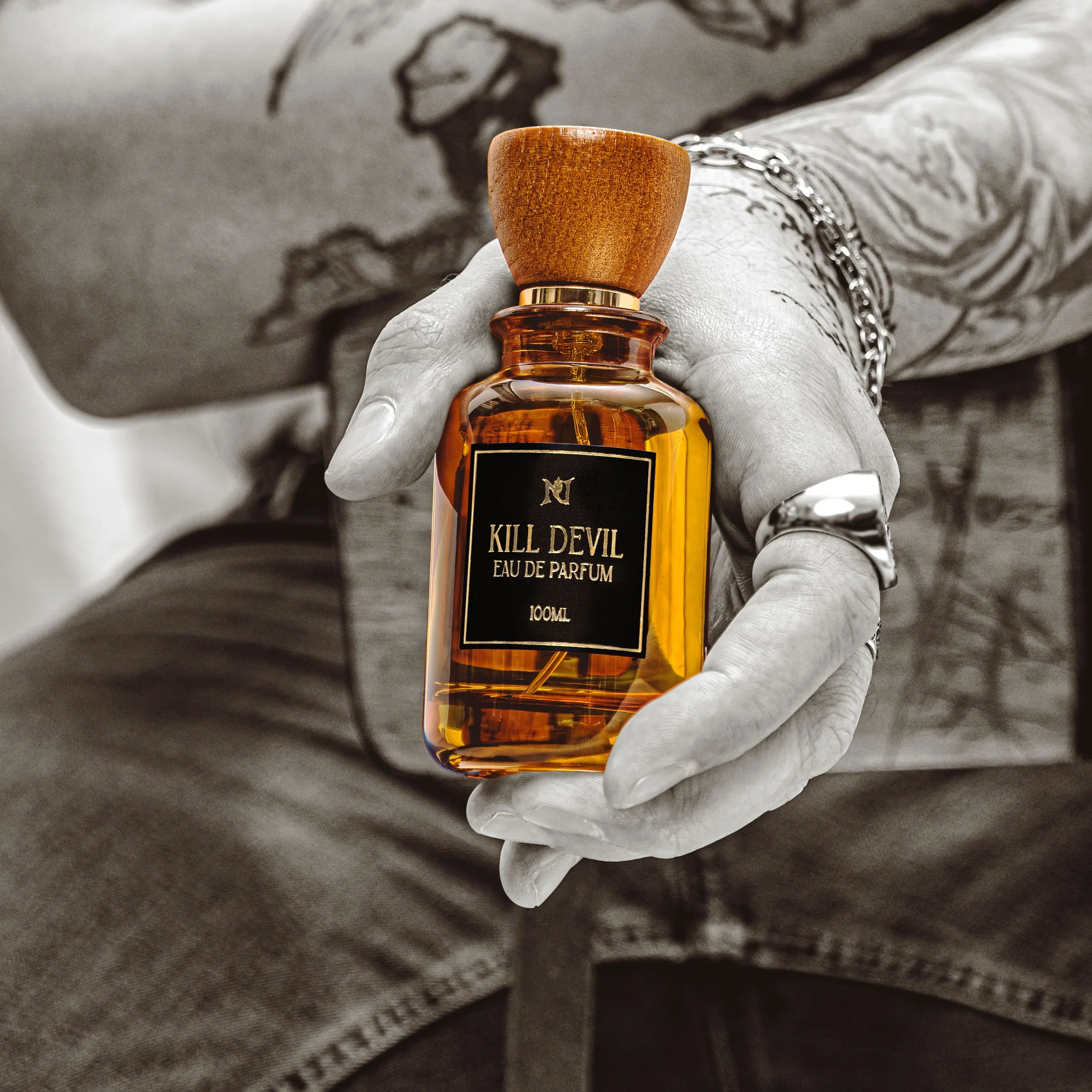 Advertising photo of a hand holding a bottle of perfume labeled 'Kill Devil Eau de Parfum,' with a gray background.