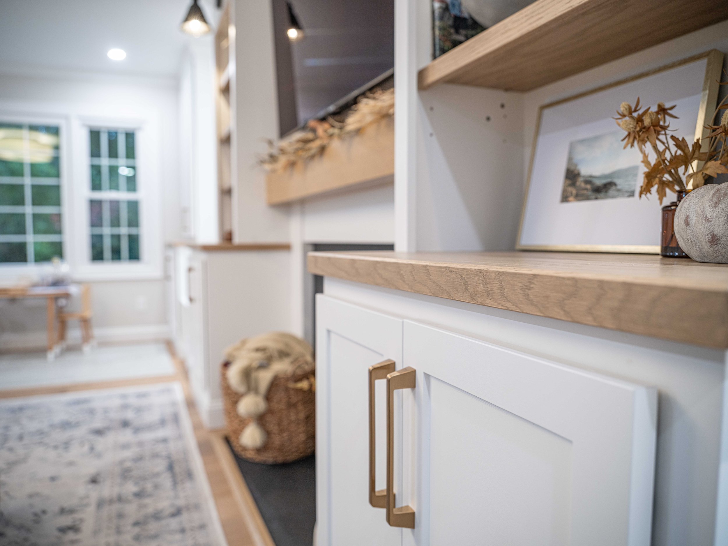 Close-up of a white kitchen cabinet with wooden countertop, gold handles, decorative framed photo, and dried floral arrangement.