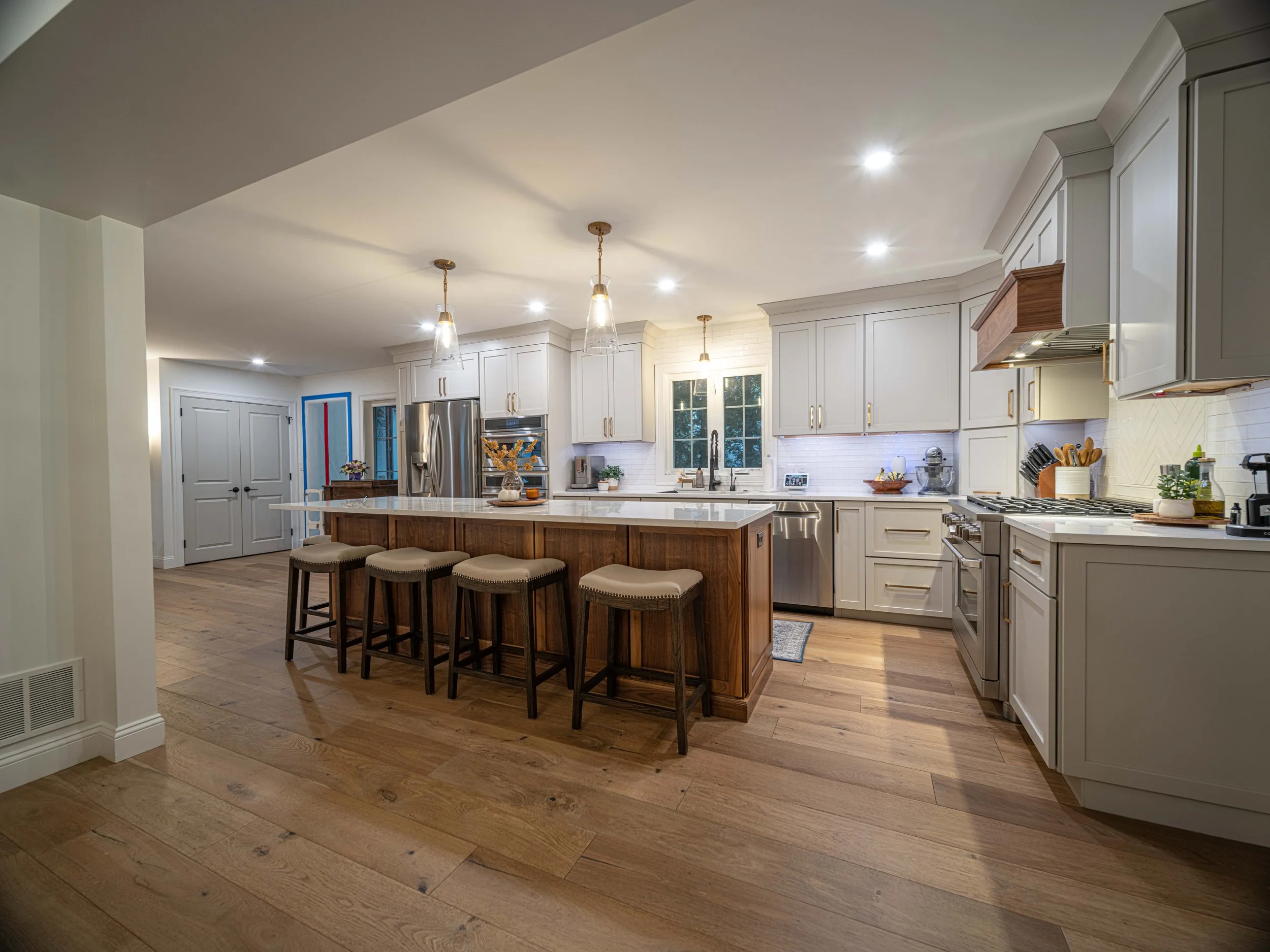 Modern kitchen with white cabinets, stainless steel appliances, a wooden island with four stools, wood flooring, and pendant lighting.