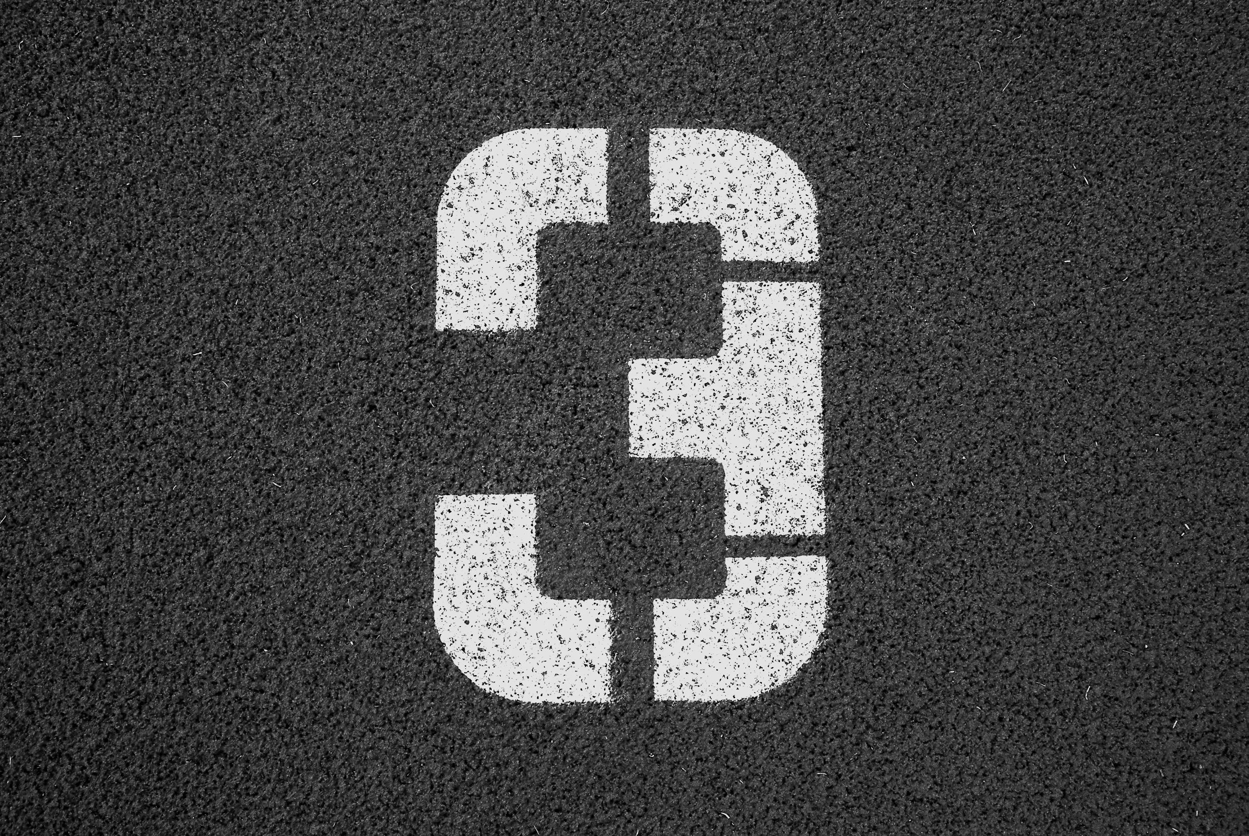 A white painted number 3 on a dark industrial surface