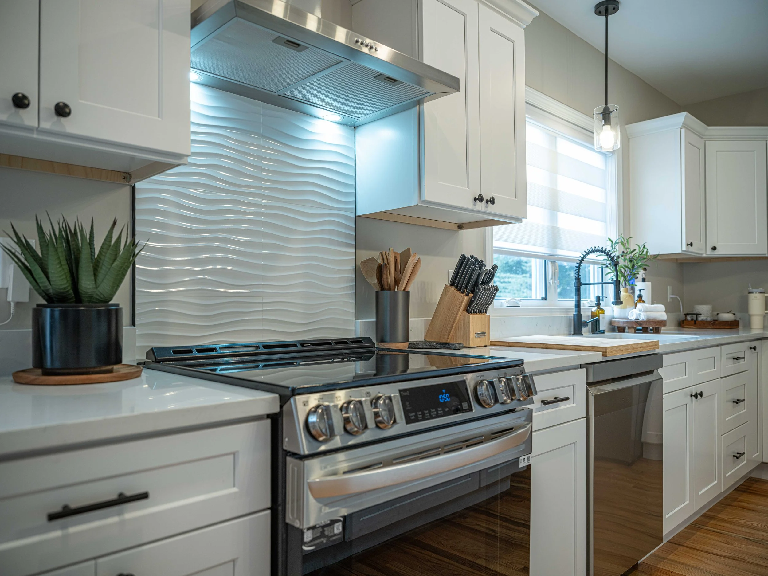 Modern kitchen with white cabinets, stainless steel stove, and decorative backsplash, next to window with a plant and kitchen utensils.
