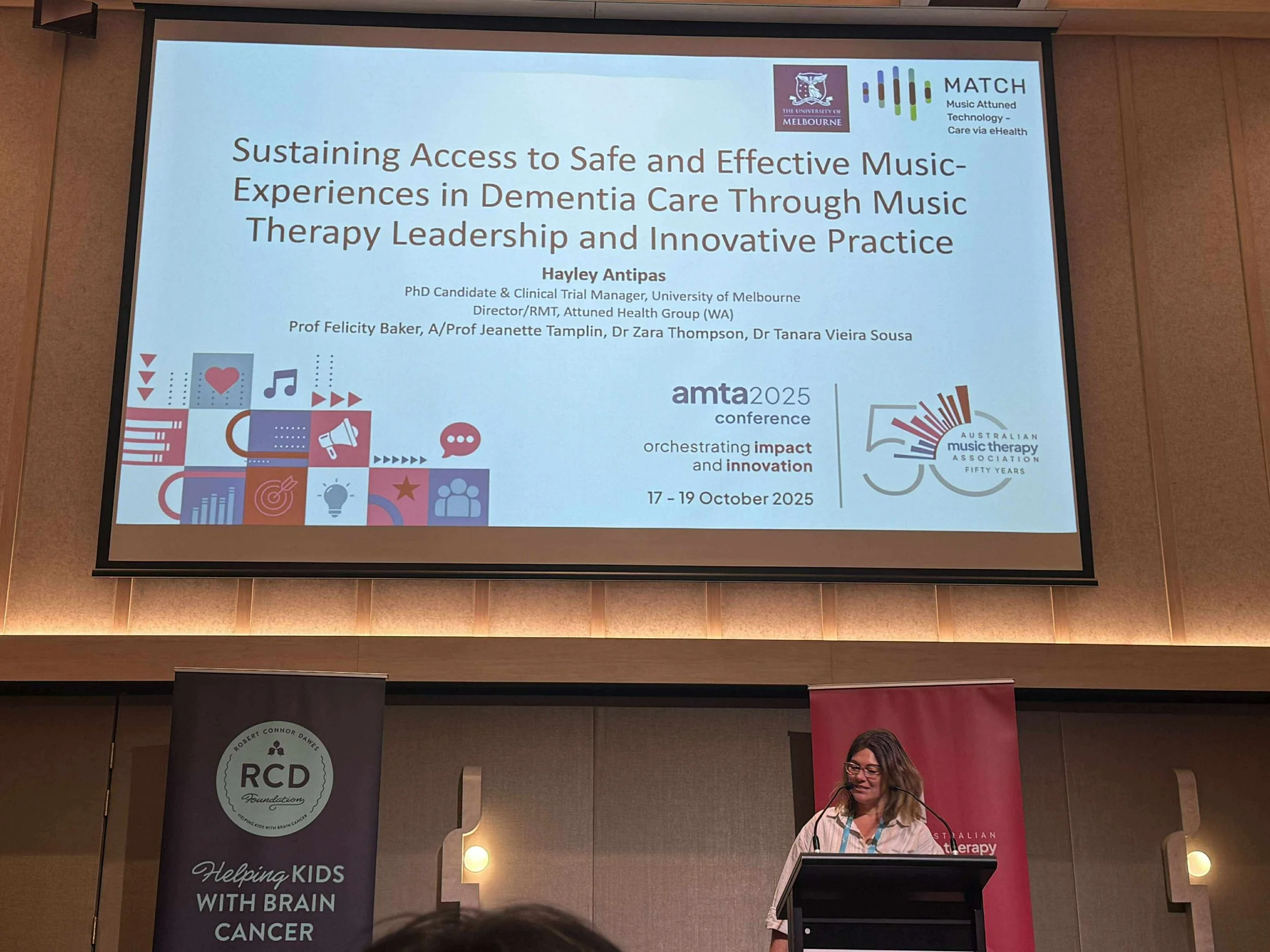 Presentation slide titled "Sustaining Access to Safe and Effective Music-Experiences in Dementia Care through Music Therapy Leadership and Innovative Practice." The slide features logos from the University of Melbourne and Australian Music Therapy Association, along with event details for the AMTA 2025 conference, and visuals including icons of music notes, a heart, and a megaphone.