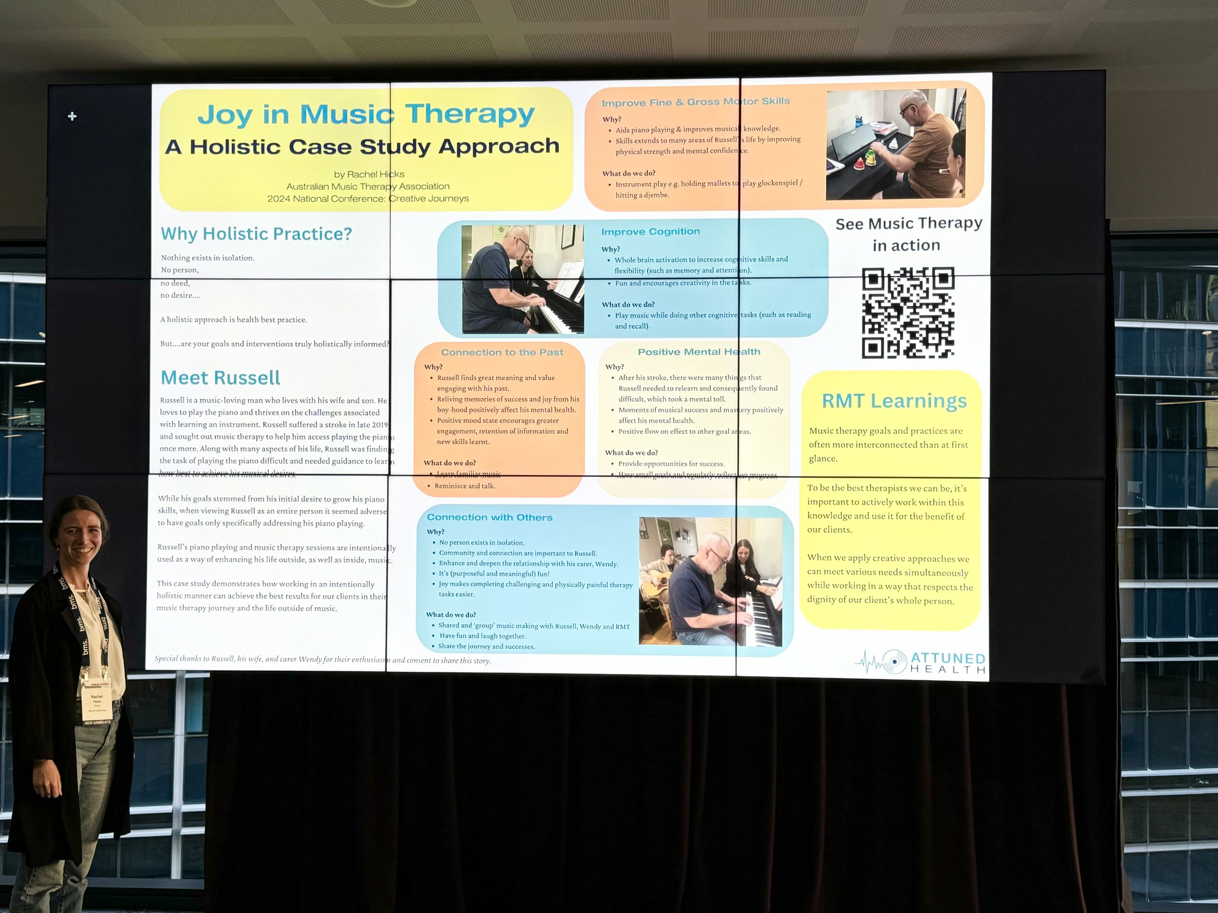 Large digital display screen showing a presentation slide titled "Joy in Music Therapy: A Holistic Case Study Approach" with multicolored text boxes and images of people playing musical instruments. A woman stands at the left, smiling, with a lanyard around her neck.