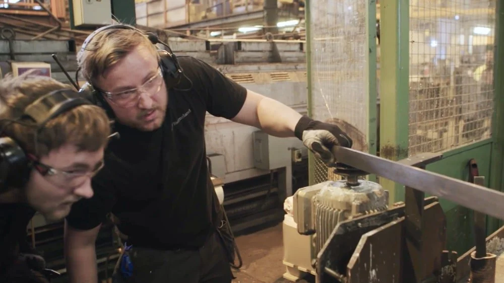 To menn i verneutstyr bruker en maskin i et industrimiljø
