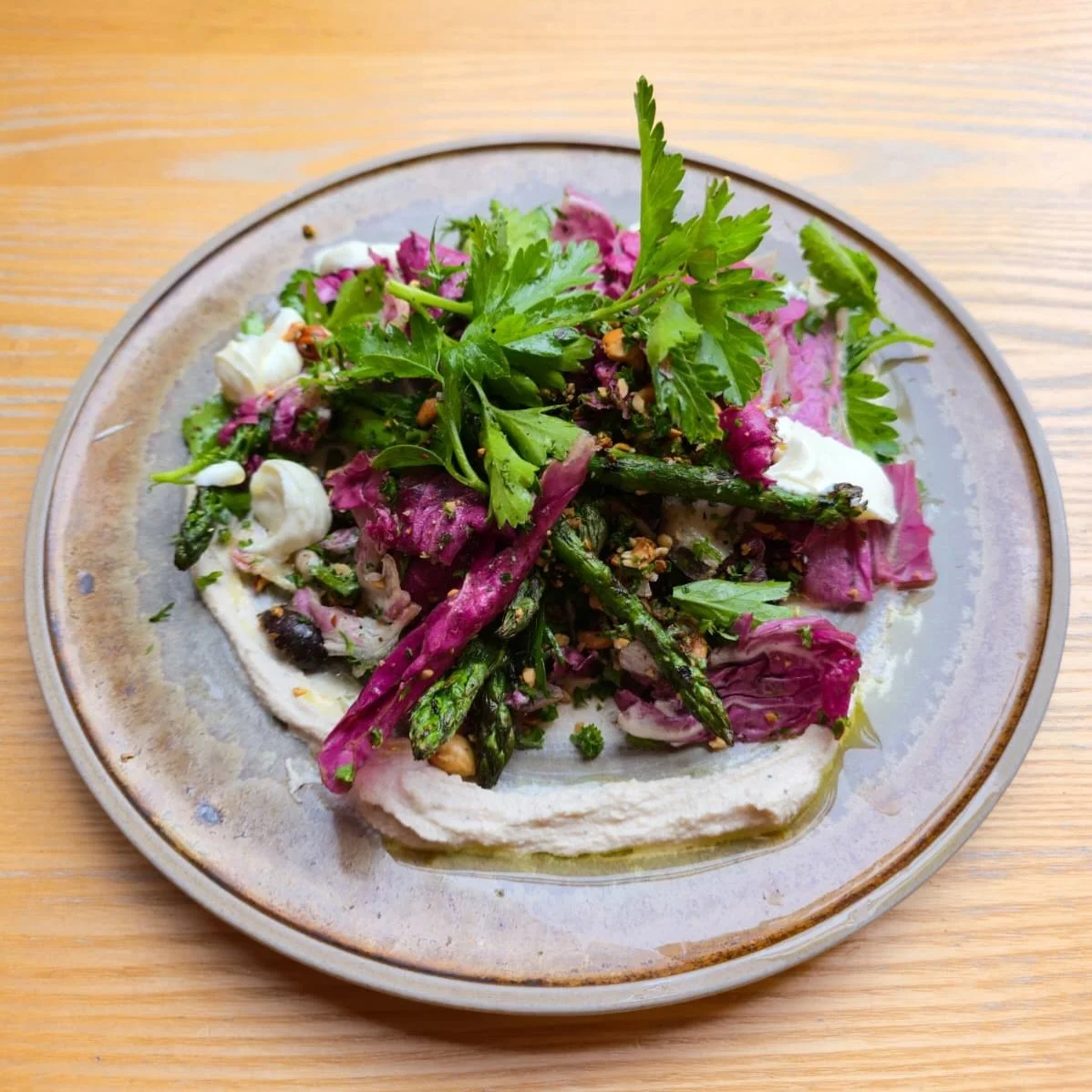 Asparagus season has arrived! Grilled asparagus served on a thick layer of whipped garlic tahini, tangy labneh,  radicchio, pulled together with the freshness of dill and parsley, the rich nutty sweetness from hazlenuts, complemented by the Kalamata 