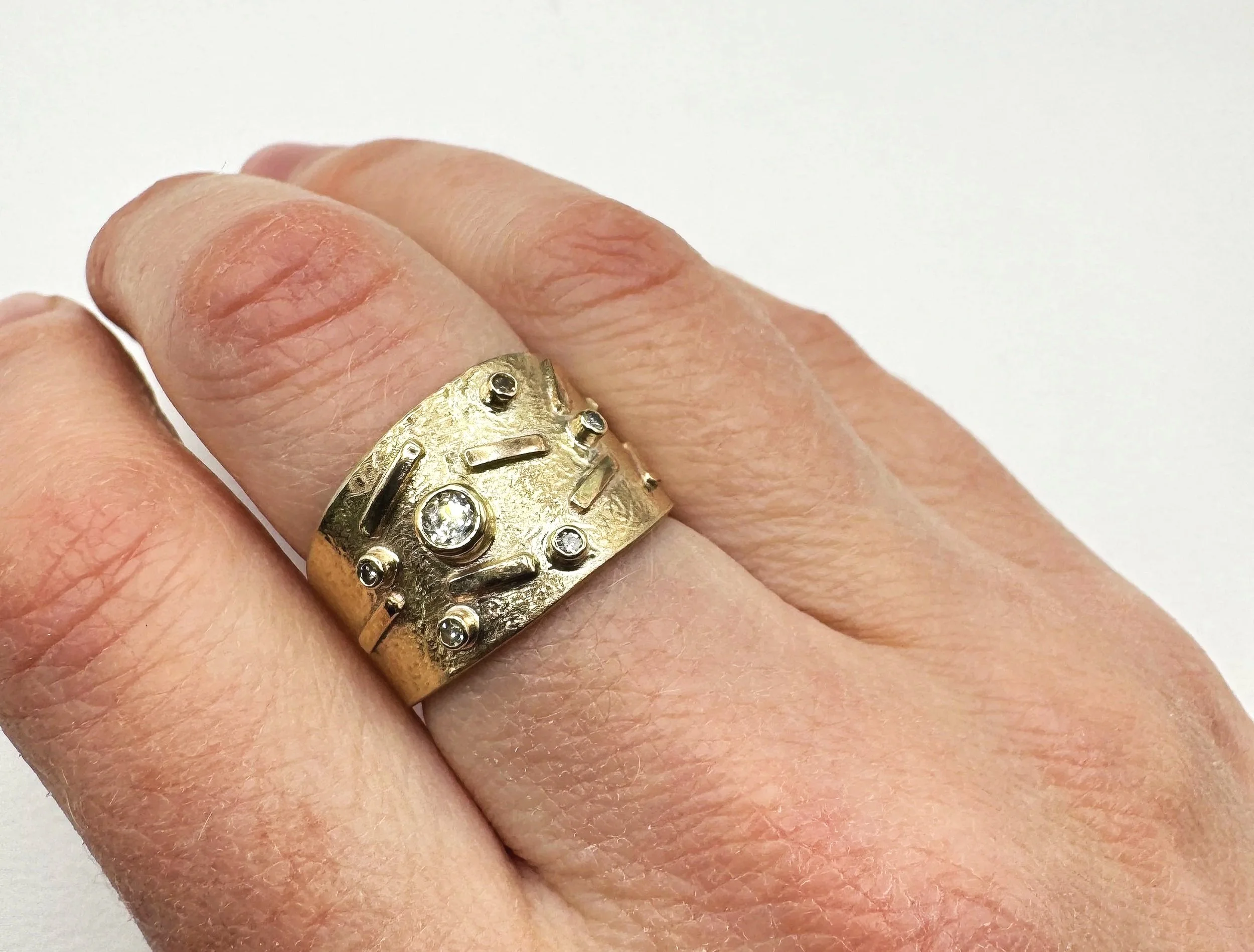 Close-up of a person's hand wearing a large gold ring with small diamonds embedded on the band.