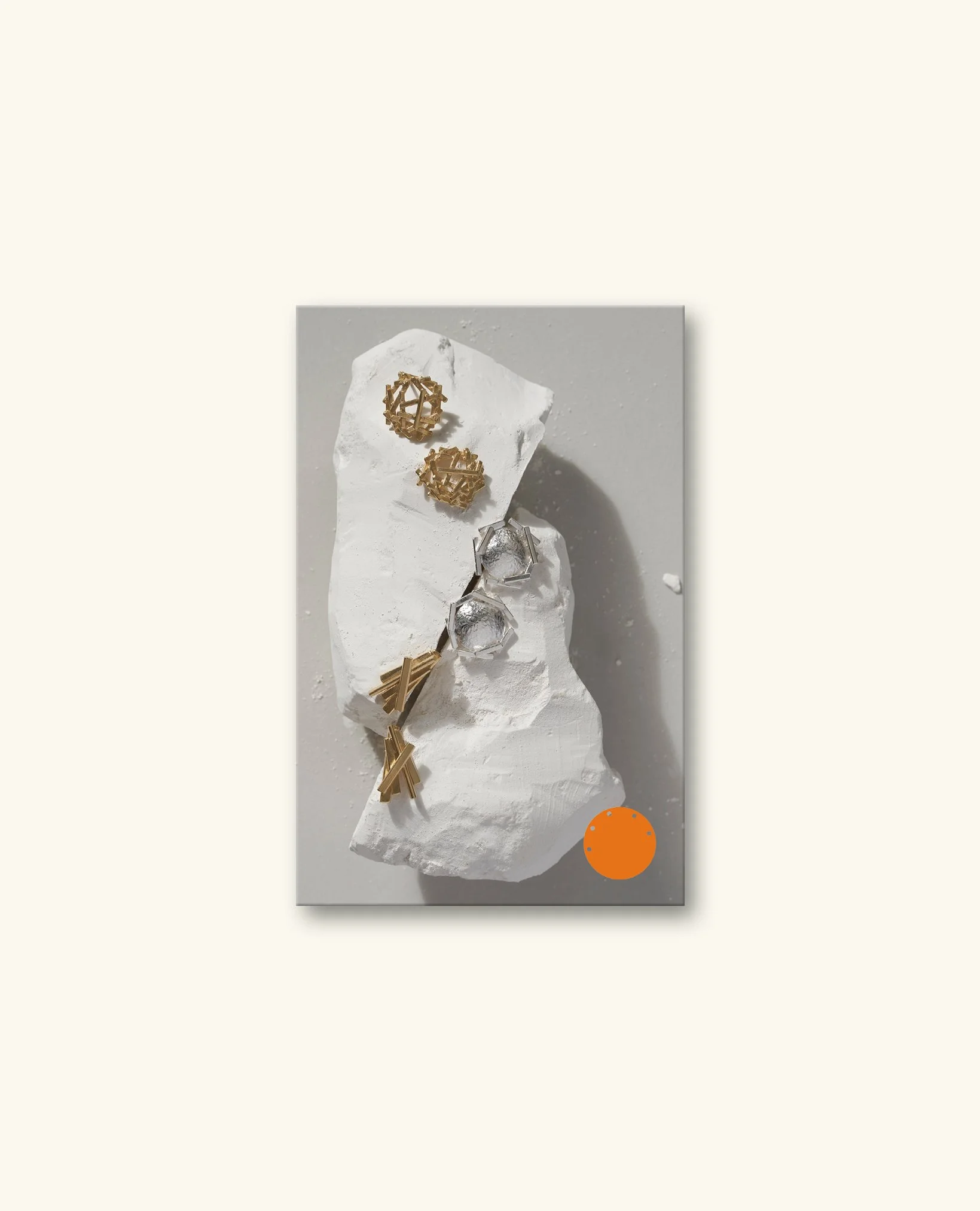 Gold geometric jewelry pieces displayed on a white textured surface with a mirror and an orange circle in the background.