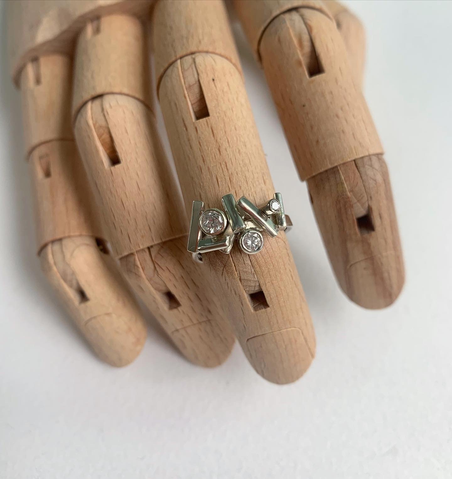 A silver ring with multiple geometric shapes and embedded clear gemstones on a wooden display finger.