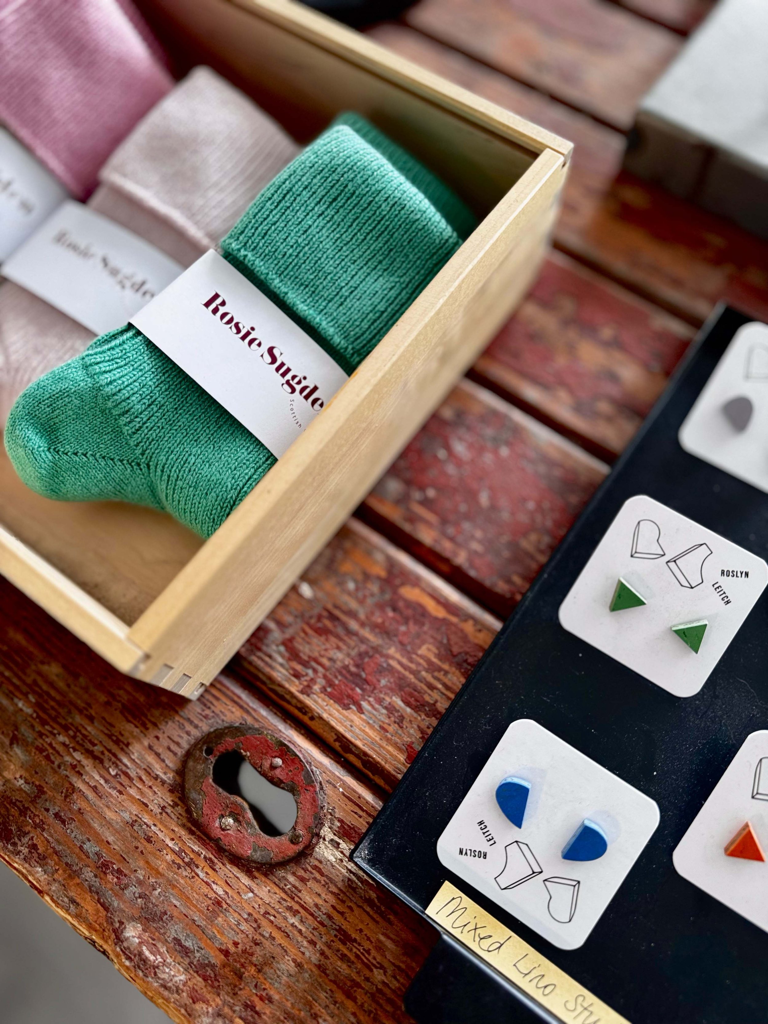 Colorful socks in a wooden box alongside a display with color samples and a label that reads 'Mixed Lino Shoe' on a wooden surface.