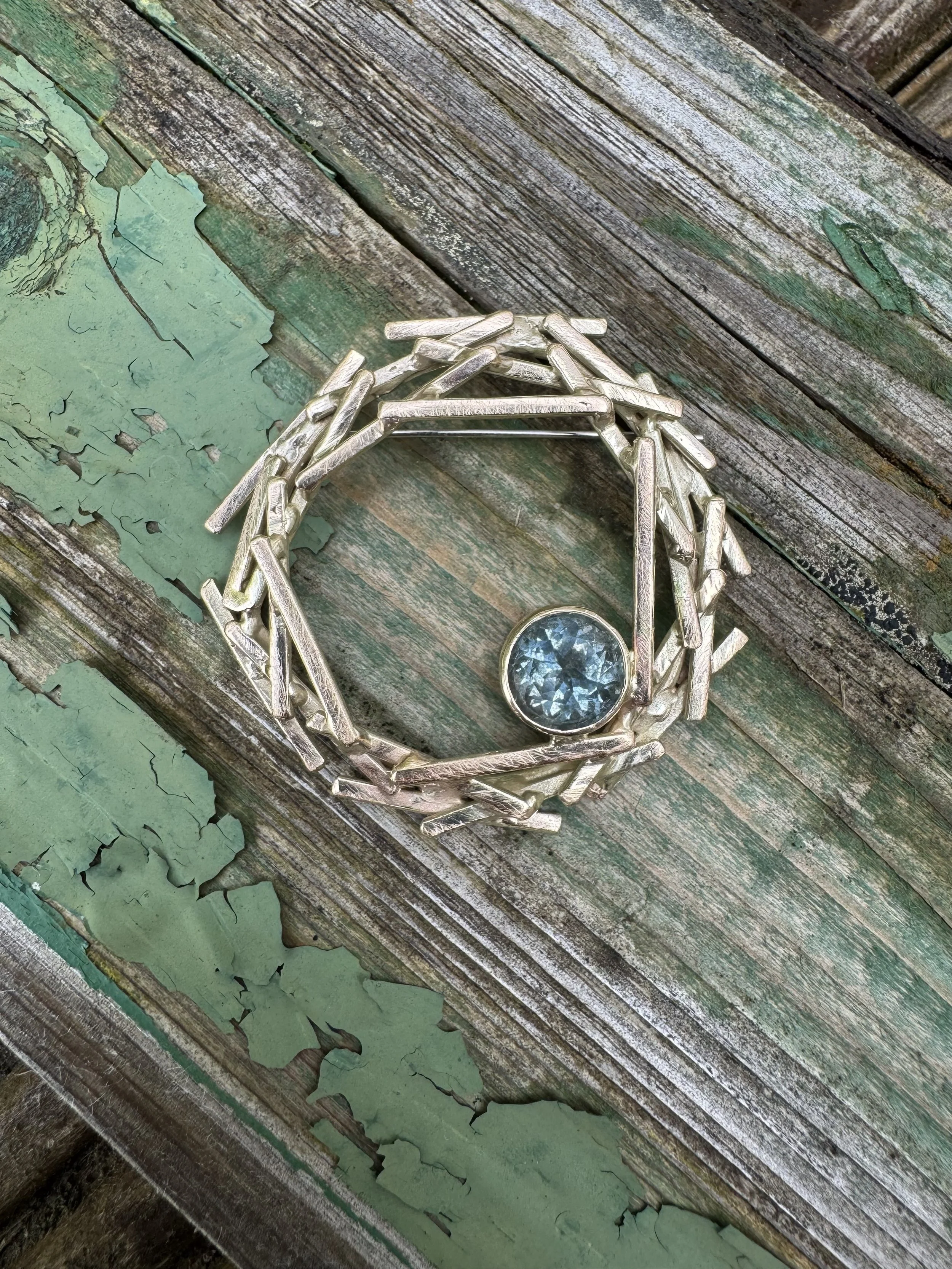 Close-up of a silver ring with a large blue gemstone on a weathered, peeling green and brown wooden surface.