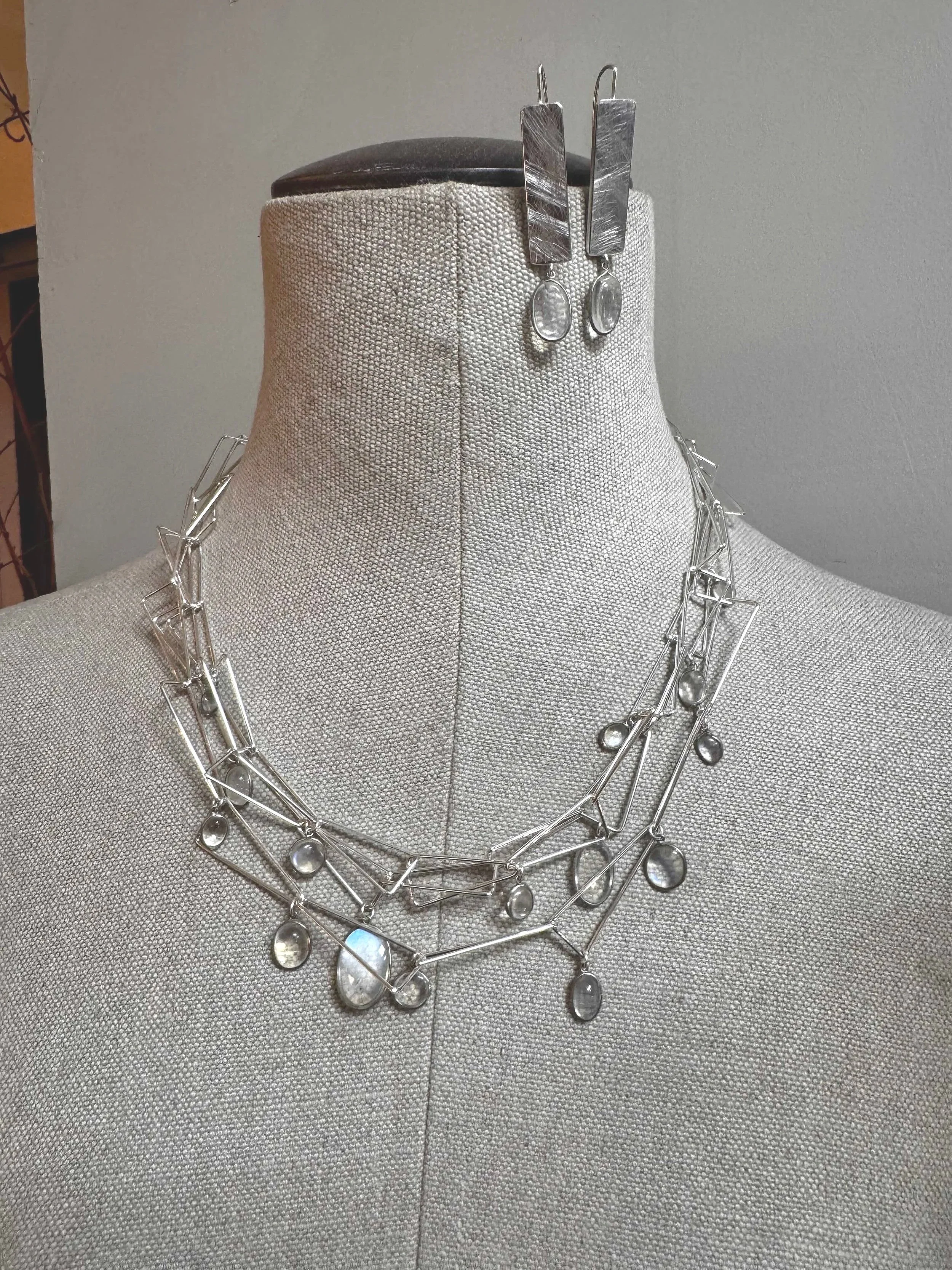 Silver jewelry necklace and earrings displayed on a beige mannequin bust.