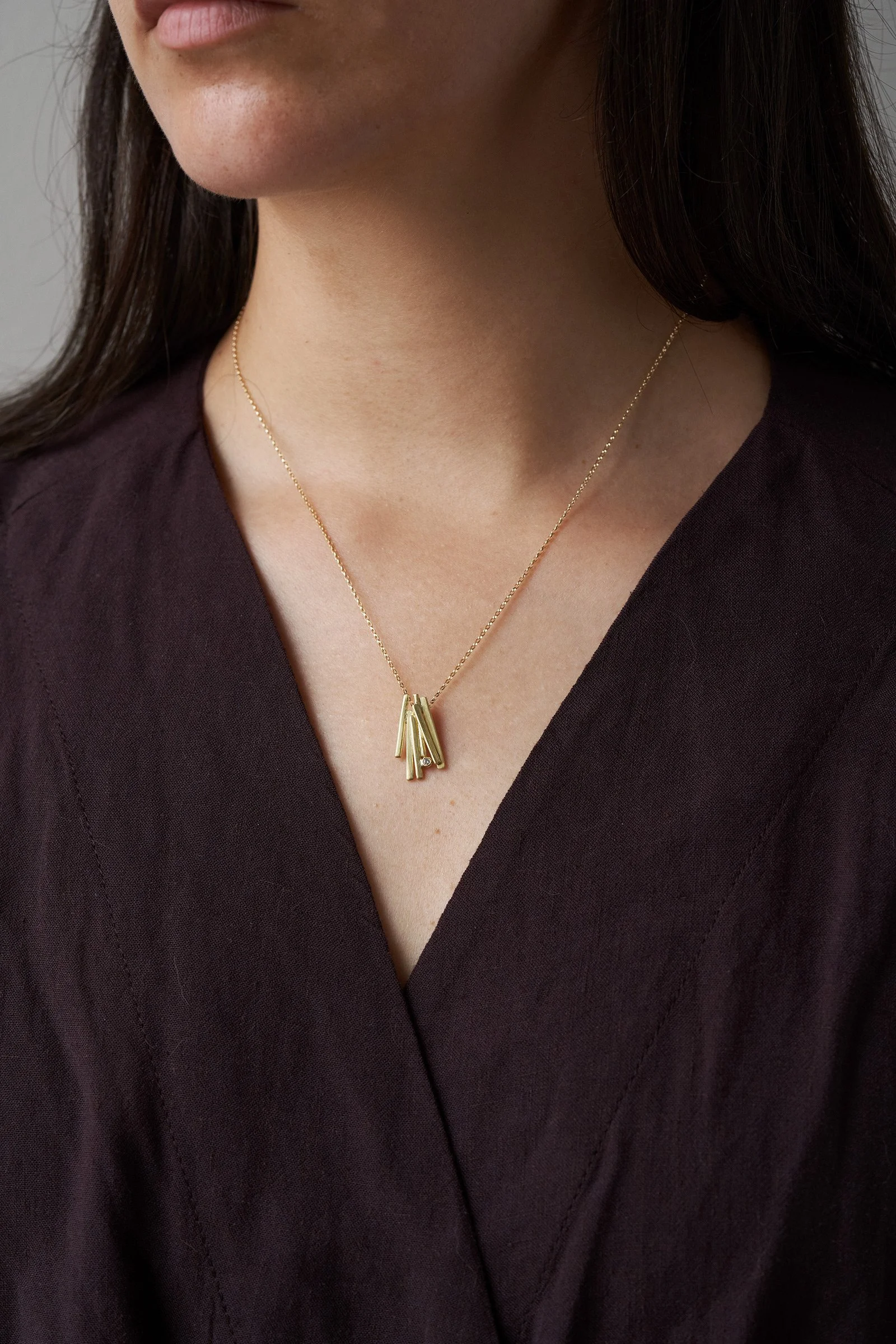 Close-up of a woman's neck and lower face, wearing a gold necklace with a pendant, dressed in a dark V-neck top.