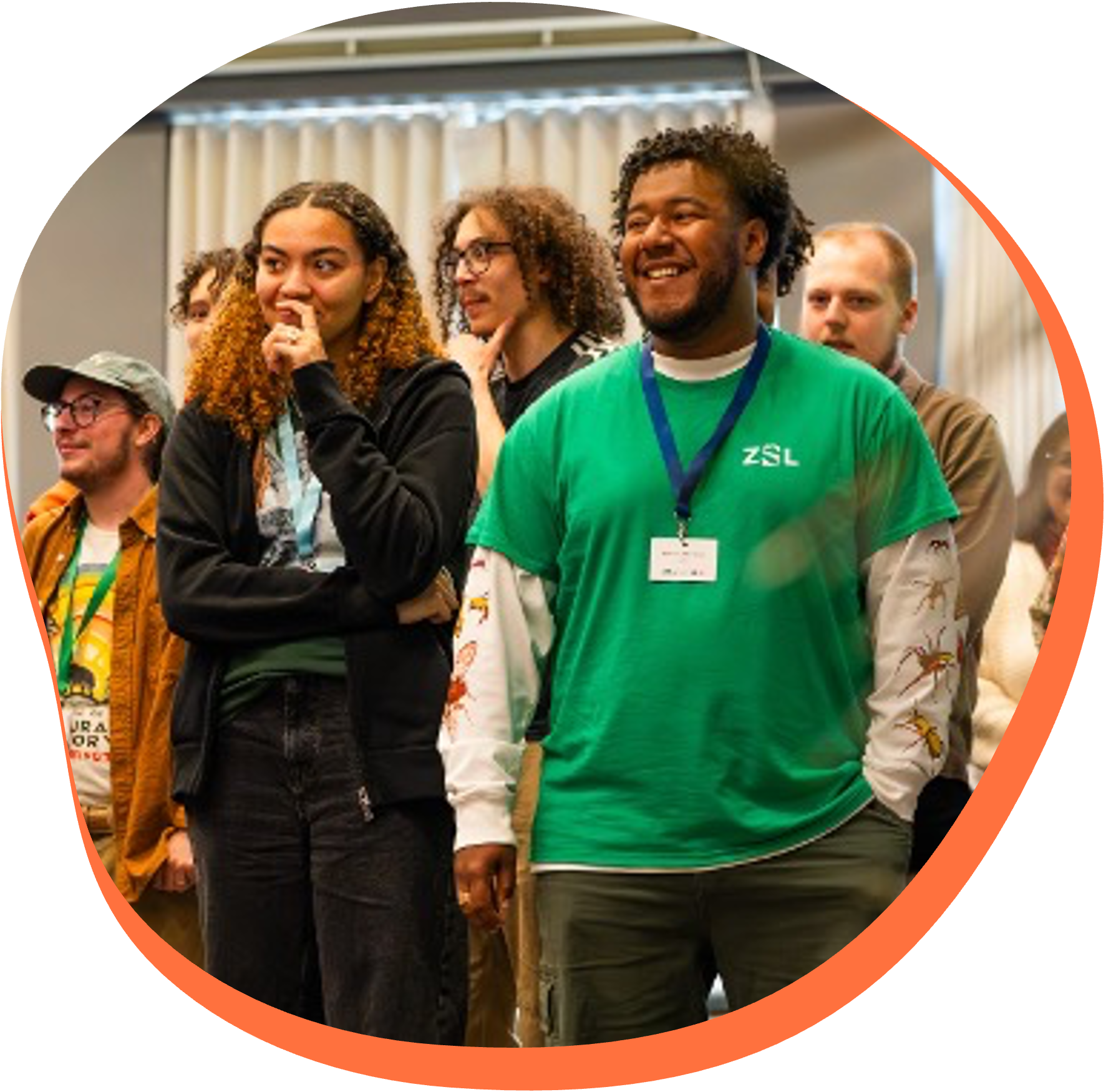 Group of diverse people attending an indoor event or conference, standing and listening attentively.
