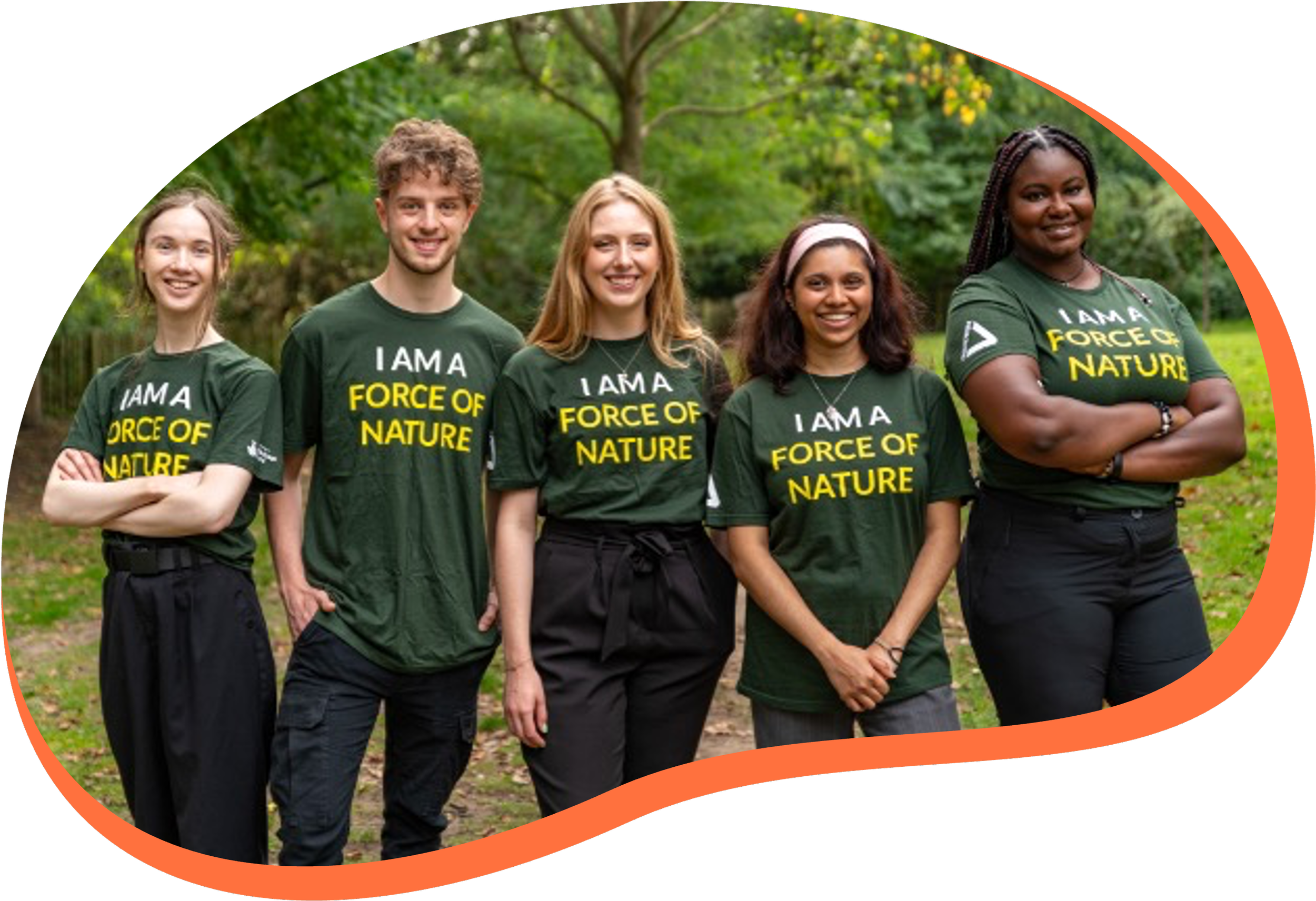 Group of five diverse women standing outdoors in a park, wearing matching green T-shirts that say 'I AM A FORCE OF NATURE,' smiling in front of green trees.