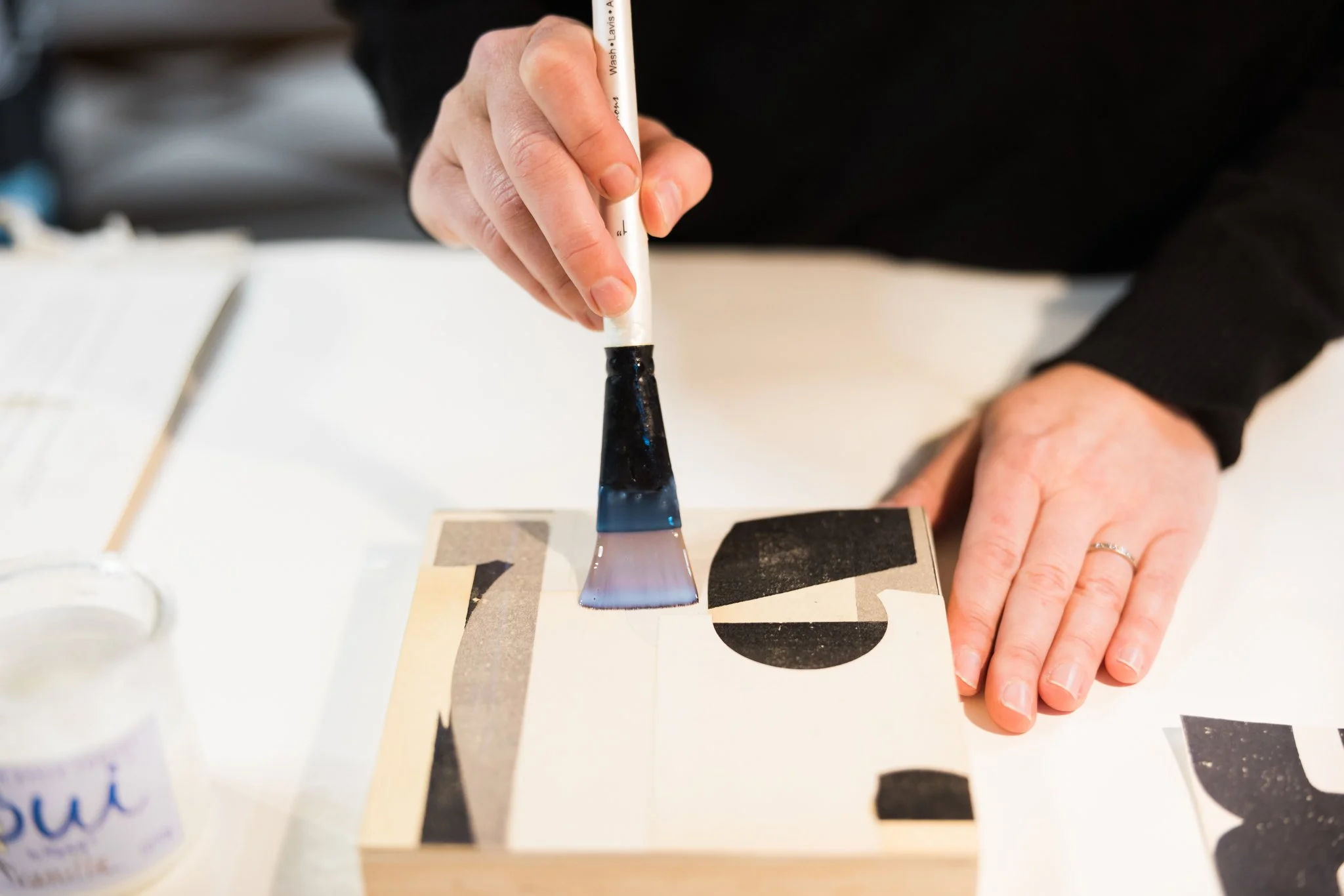 Person using a brush to apply adhesive onto a piece of abstract art with geometric shapes.