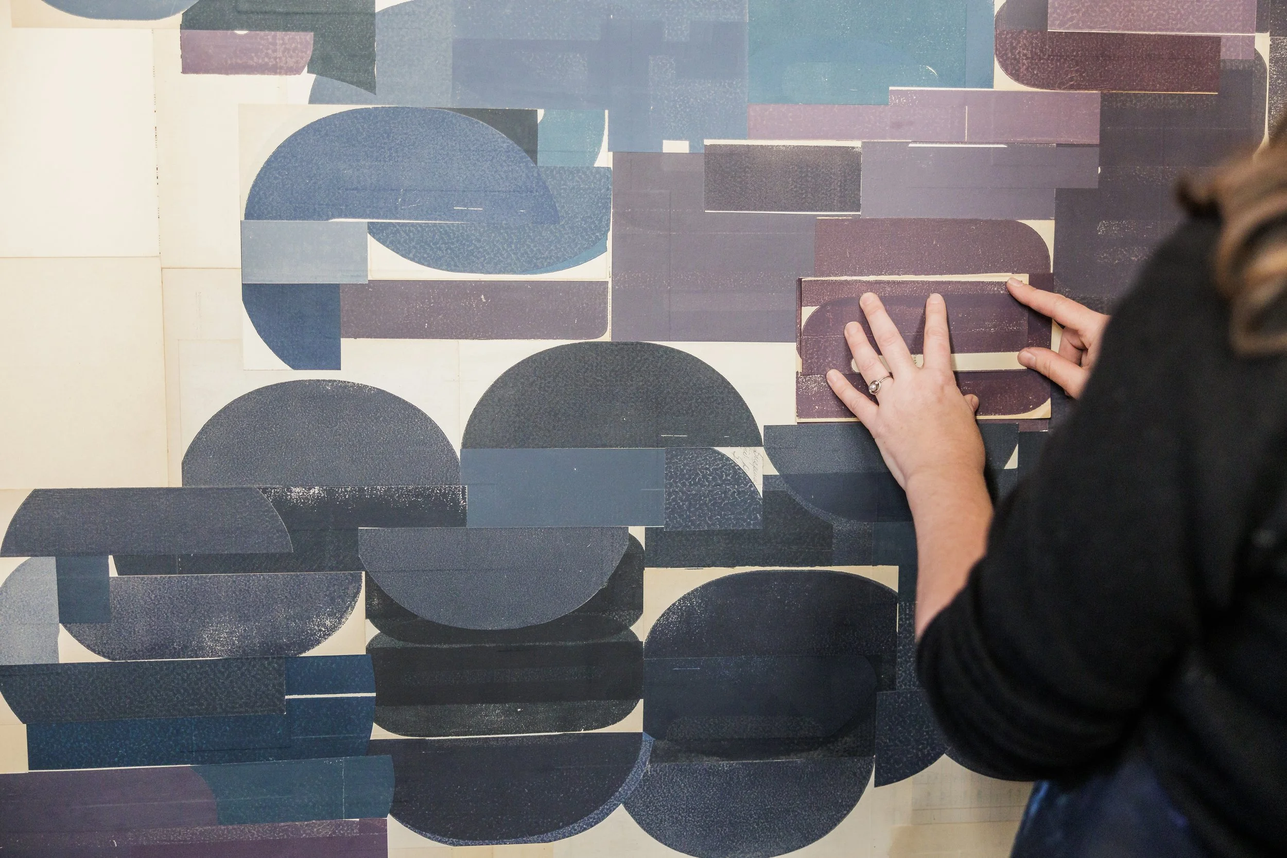 Person arranging geometric blue and purple shapes on a wall.