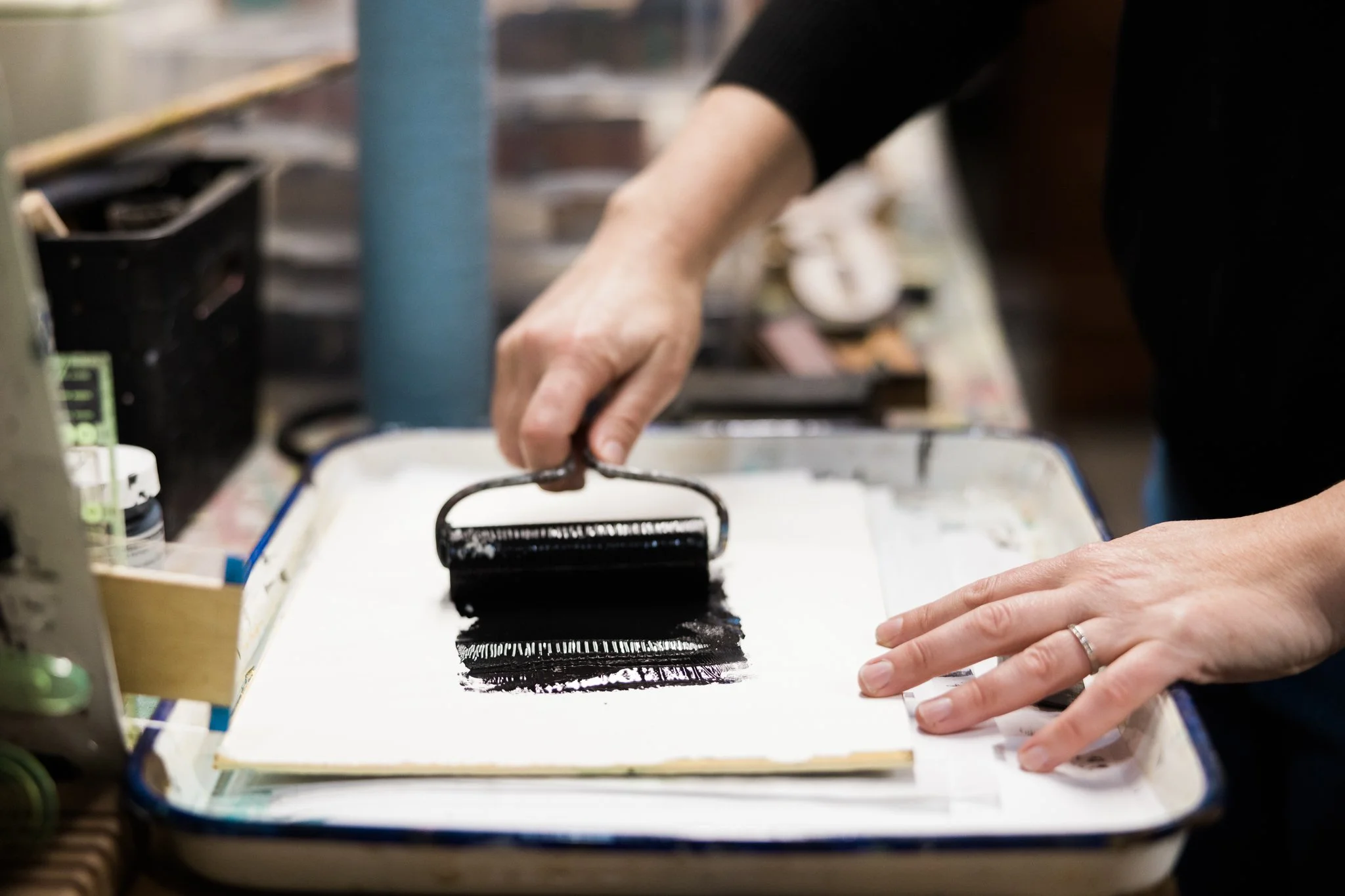 Person using a brayer to roll black ink onto a piece of paper in an art studio.