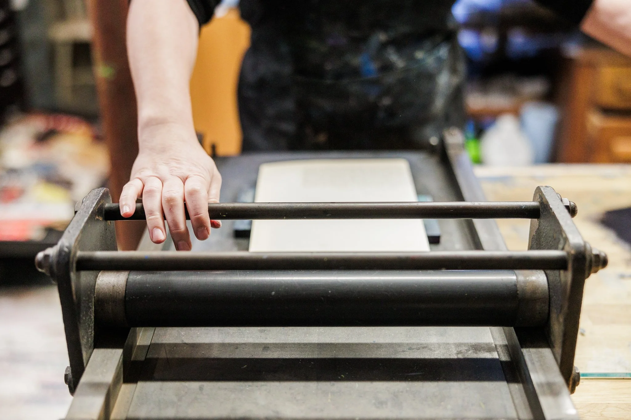 A person pressing down on a metal printmaking press in a workshop.
