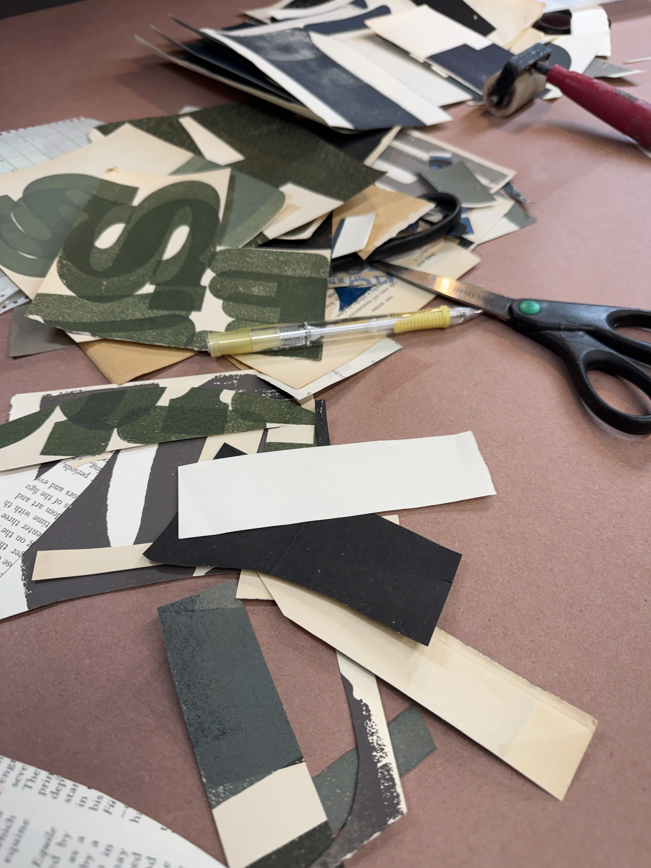 A cluttered work surface with torn paper scraps, scissors, a utility knife, and a pen scattered across a pinkish-brown table.