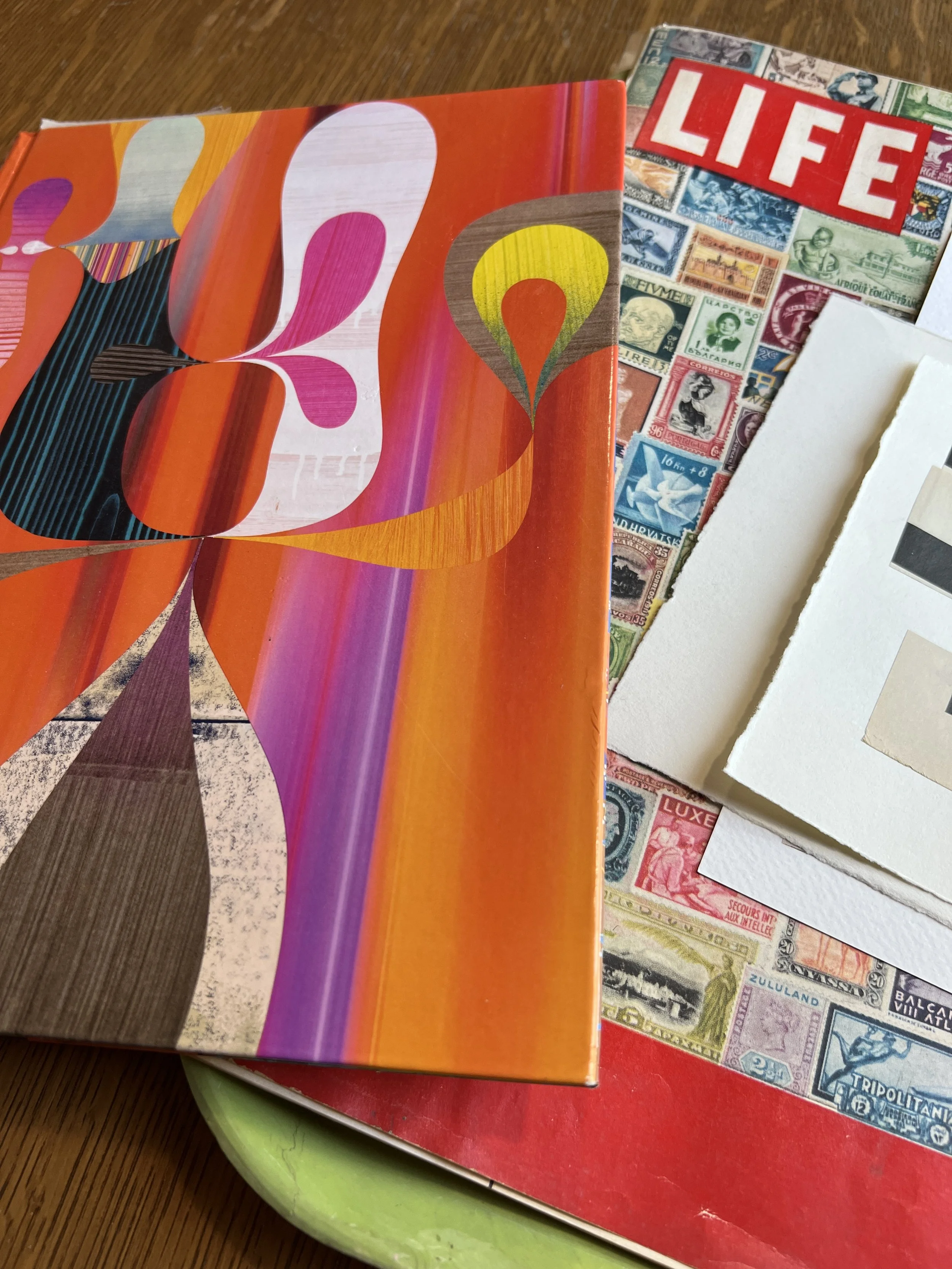 A colorful abstract art book cover and a vintage LIFE magazine with a stamp collage on a table.