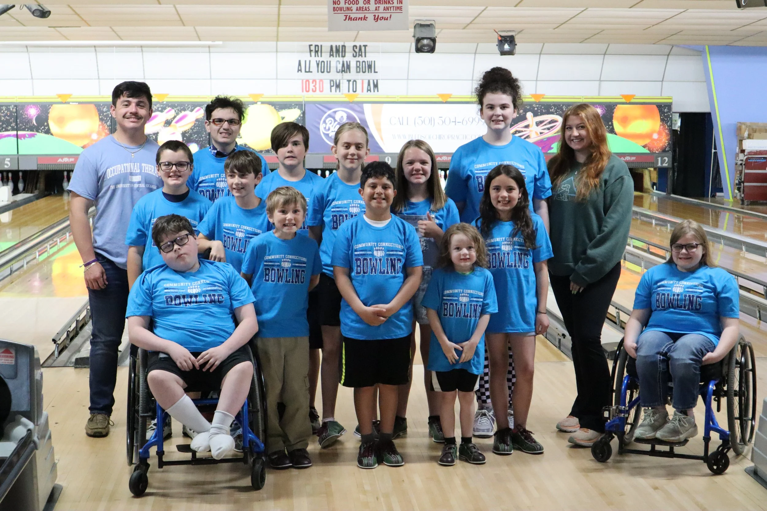children and volunteers posing in a bowling alley with matching blue shirts